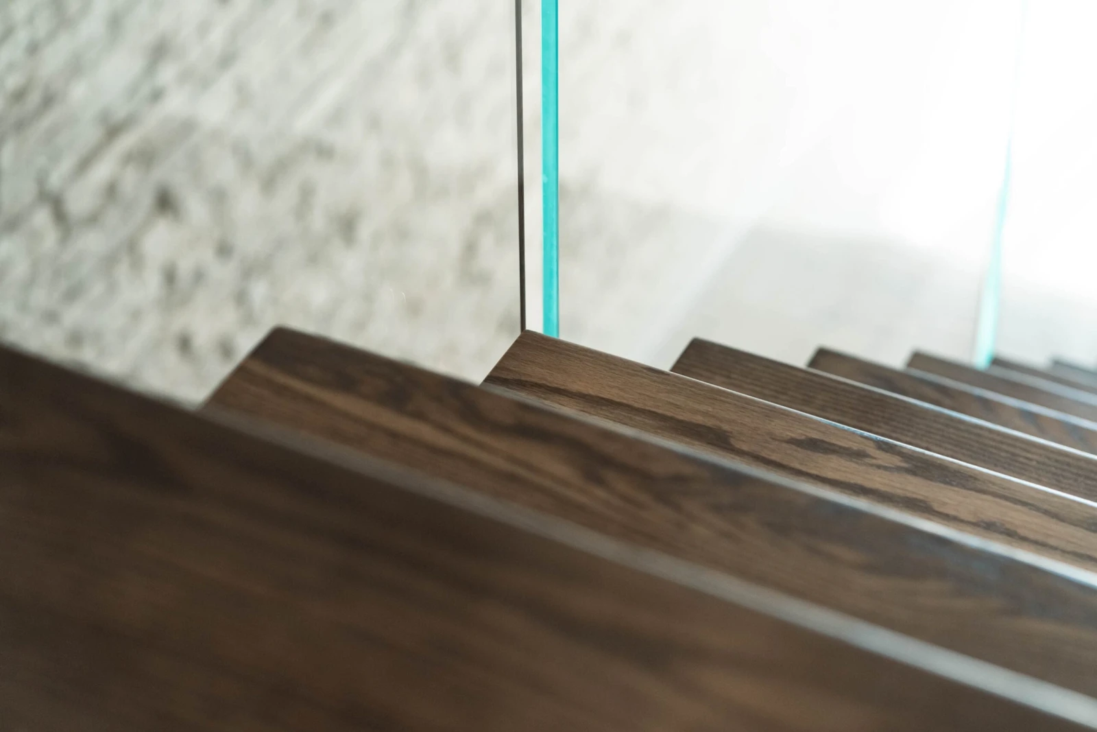 Dark-stained floating treads catch light beside the clear edge of a glass panel