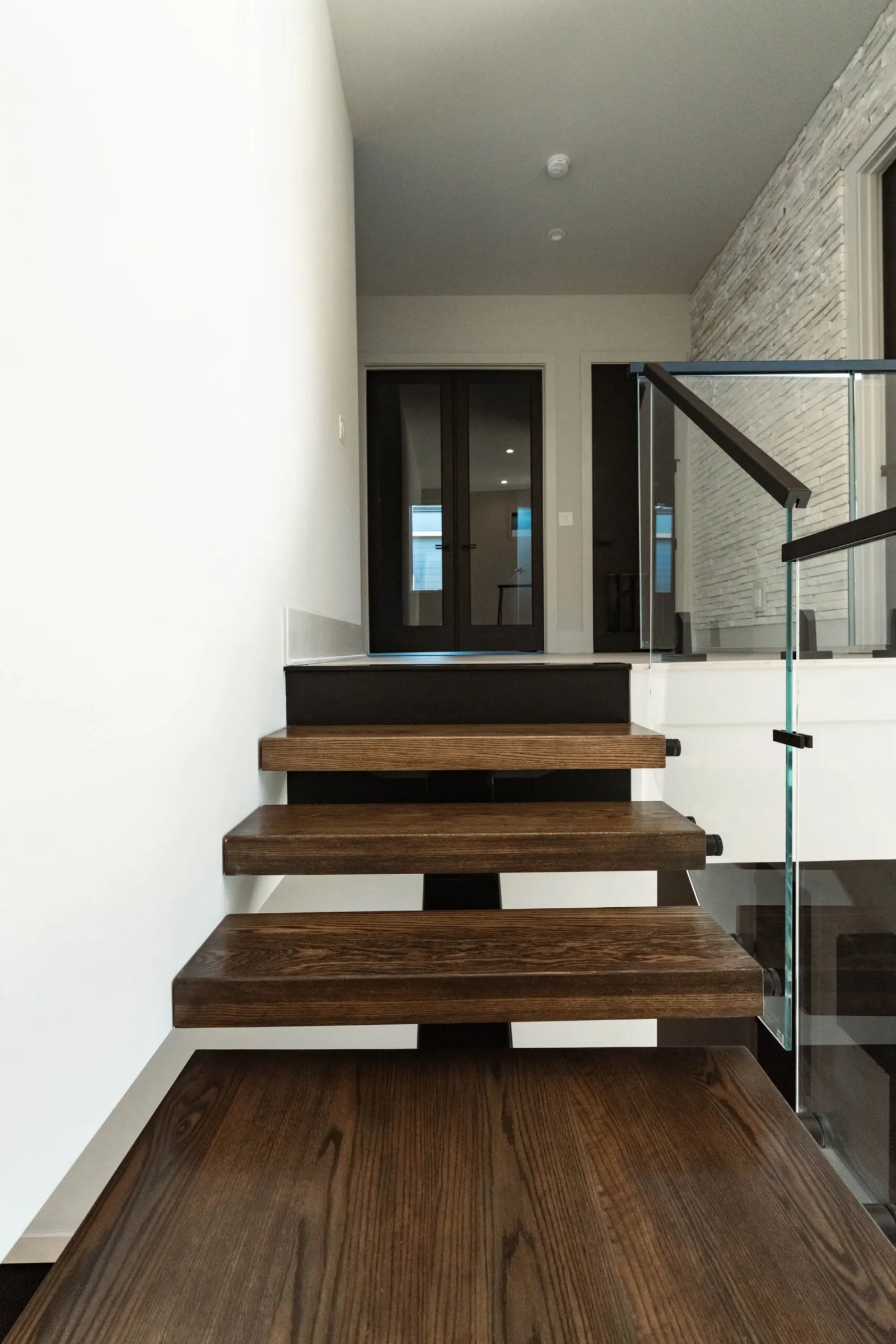 Lower flight of floating treads with glass railing and a black handrail above