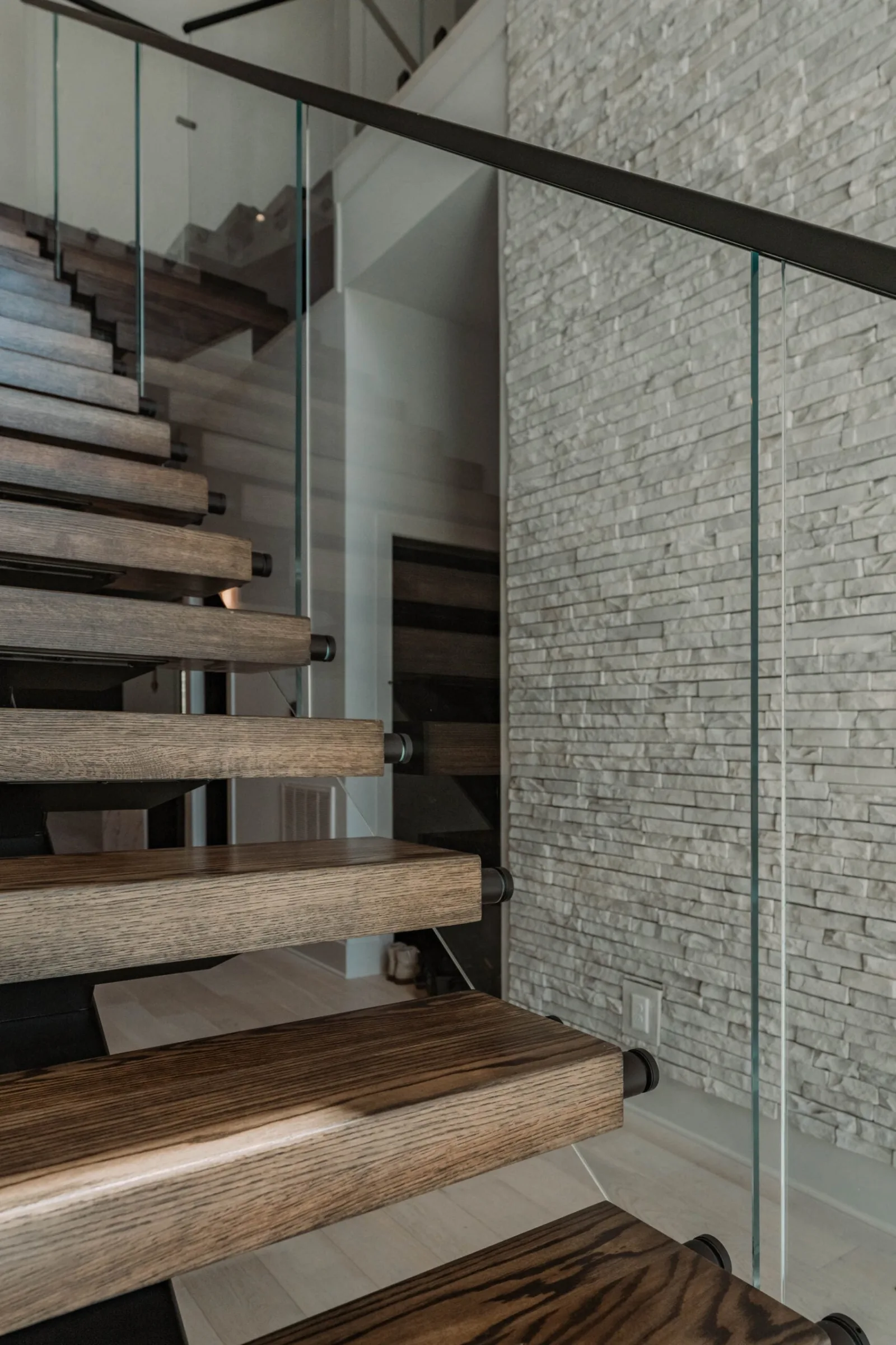 Floating stair beside a stacked stone wall with glass panels and dark treads