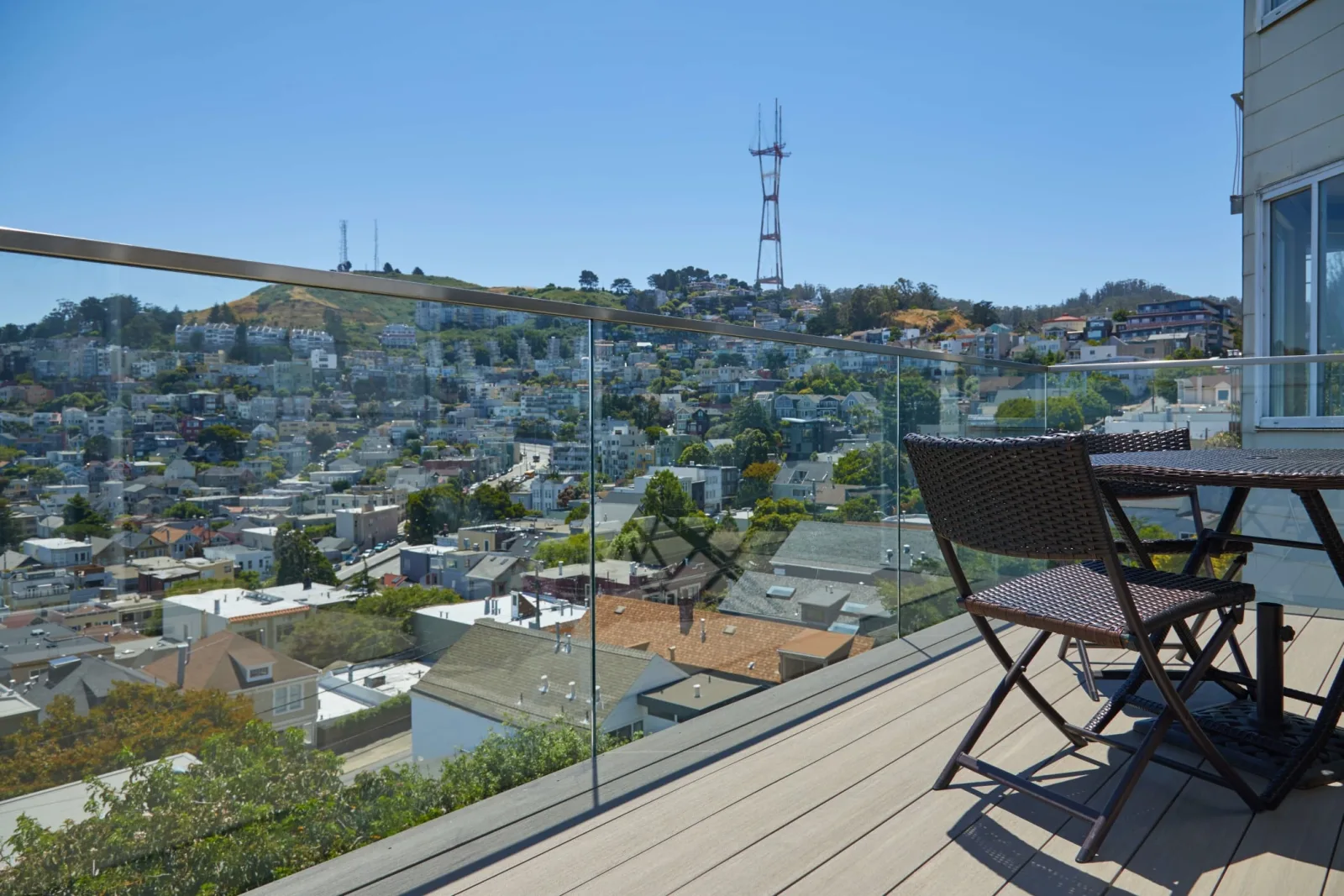 Frameless glass railing on a deck with a bistro set above a sunlit hillside neighborhood