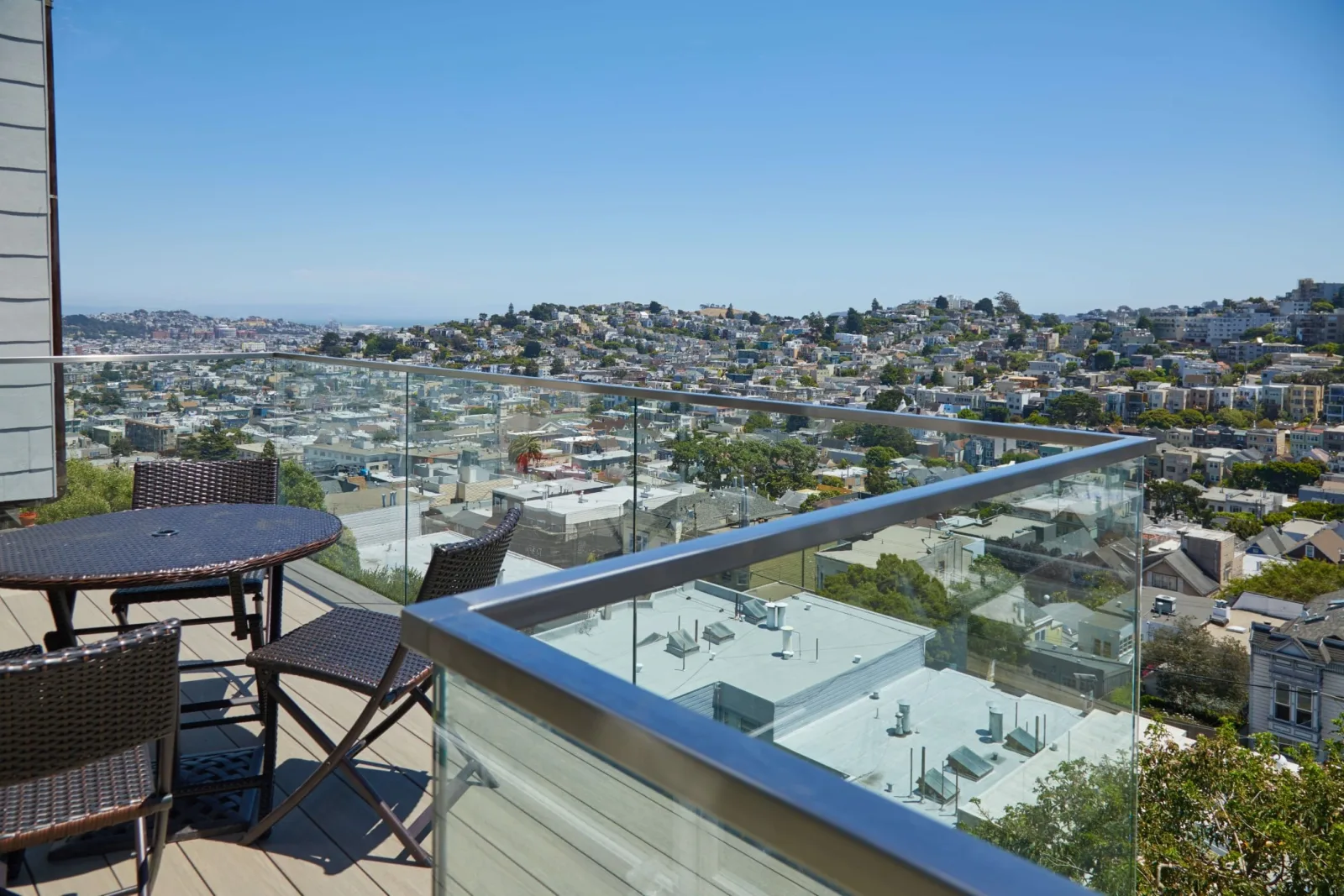 Rooftop deck seating behind a glass railing capped in stainless above a hillside city