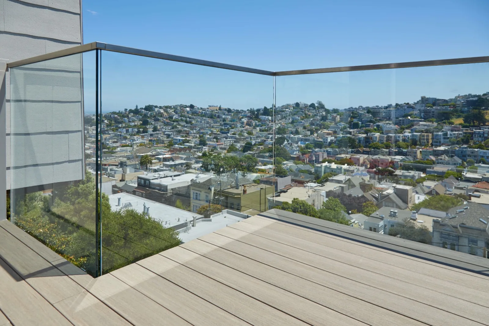Frameless glass railing wraps a roof deck corner with rooftops stretching beyond