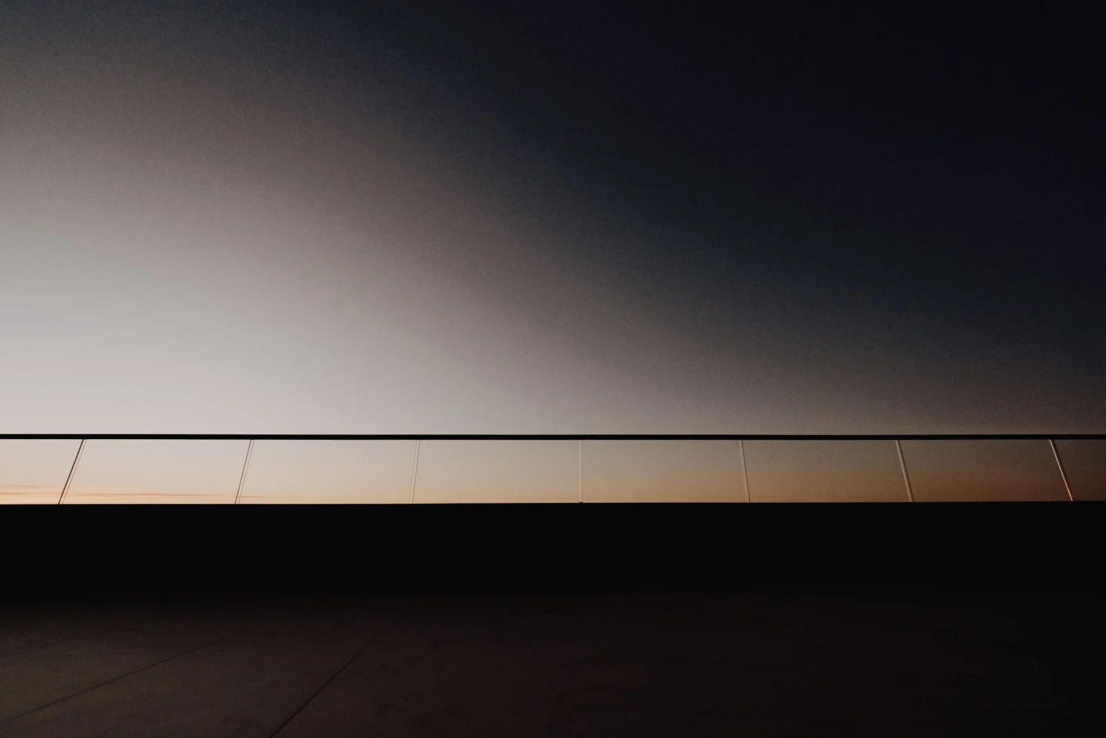 Glass railing running the full terrace edge, lit low against a deepening dusk sky