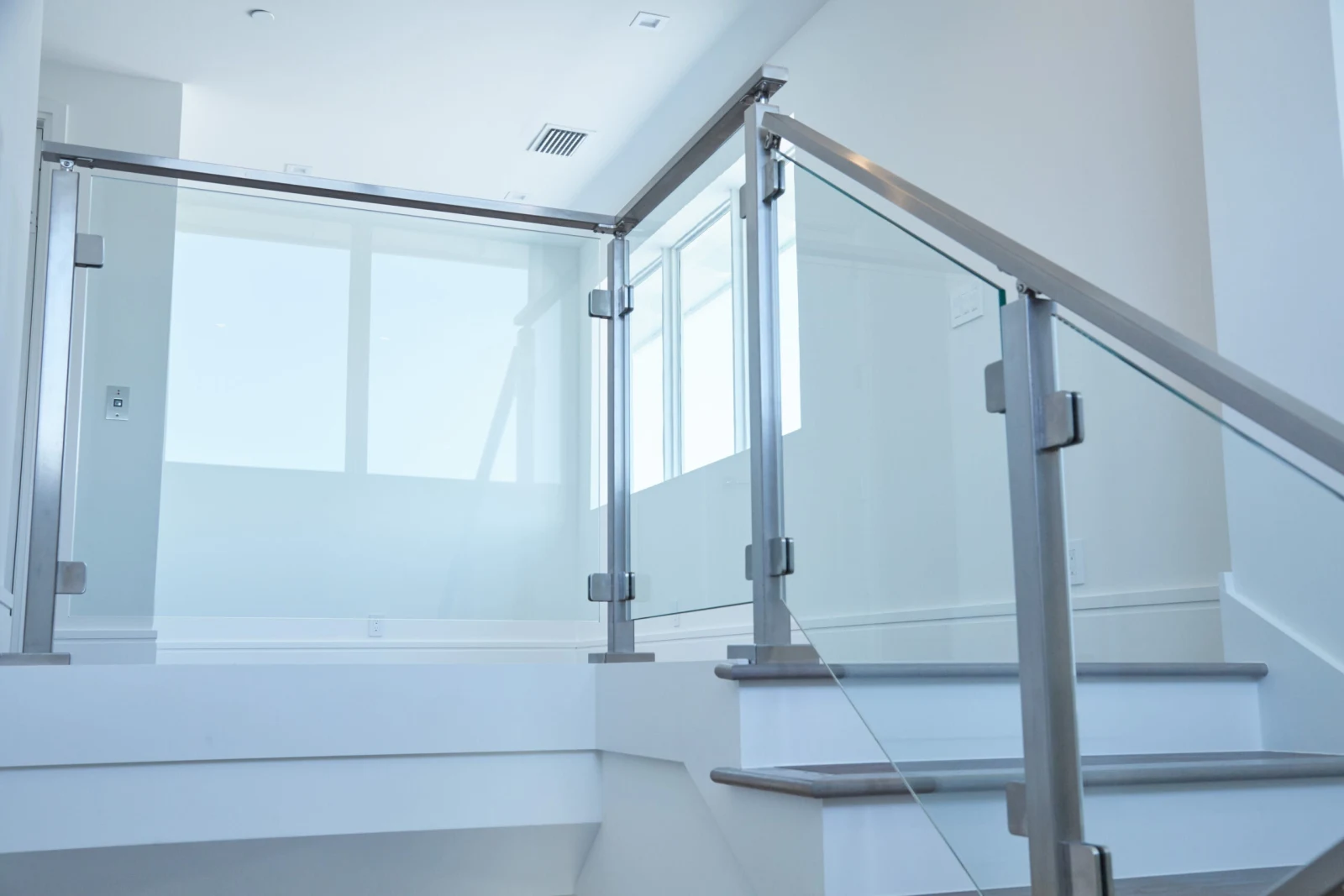 Square metal posts and glass panels guarding a landing with wall-mounted handrail