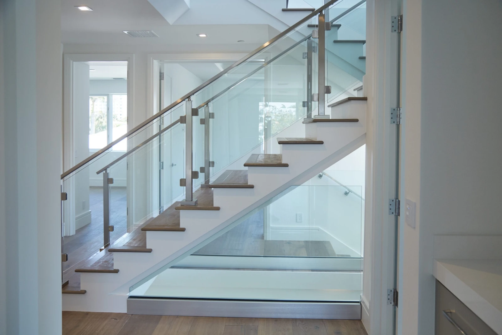 Slim metal posts hold glass panels up a straight stair in a bright white hallway