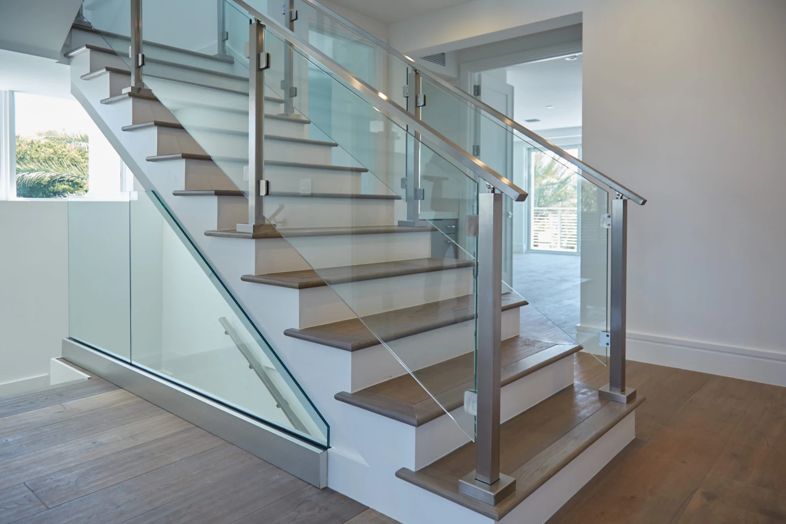 Stair rising from a wood floor behind glass panels set in slim metal posts