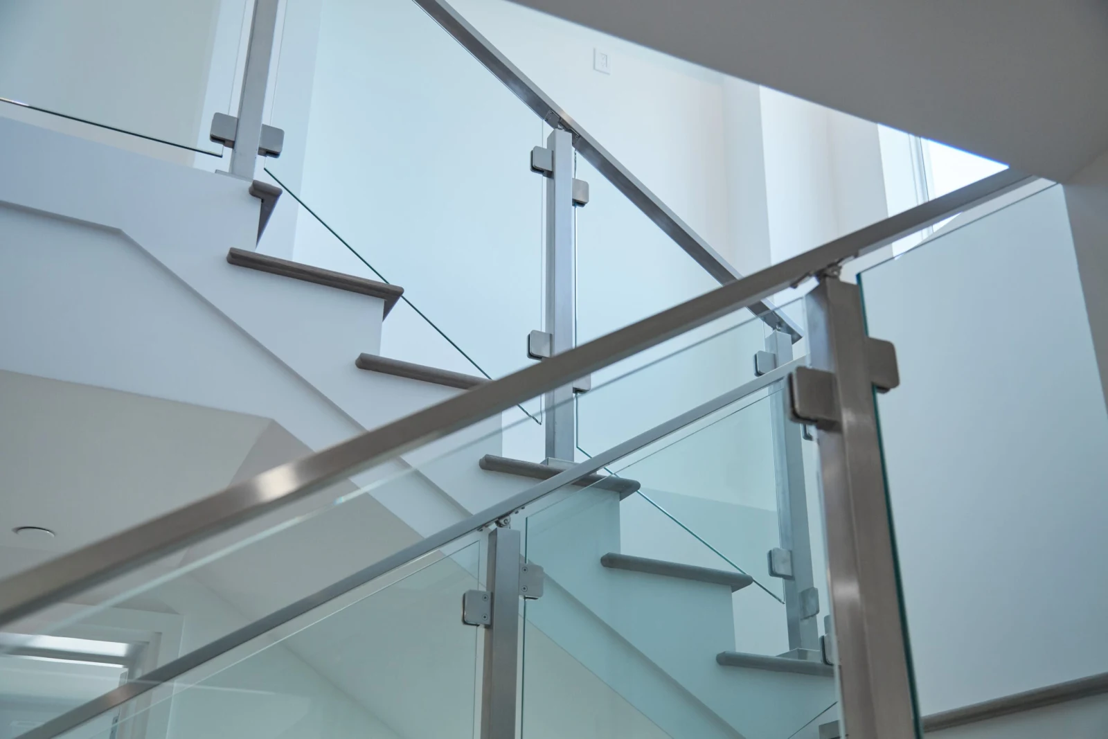 Upward angle showing brushed metal posts, glass clamps and handrails crossing overhead