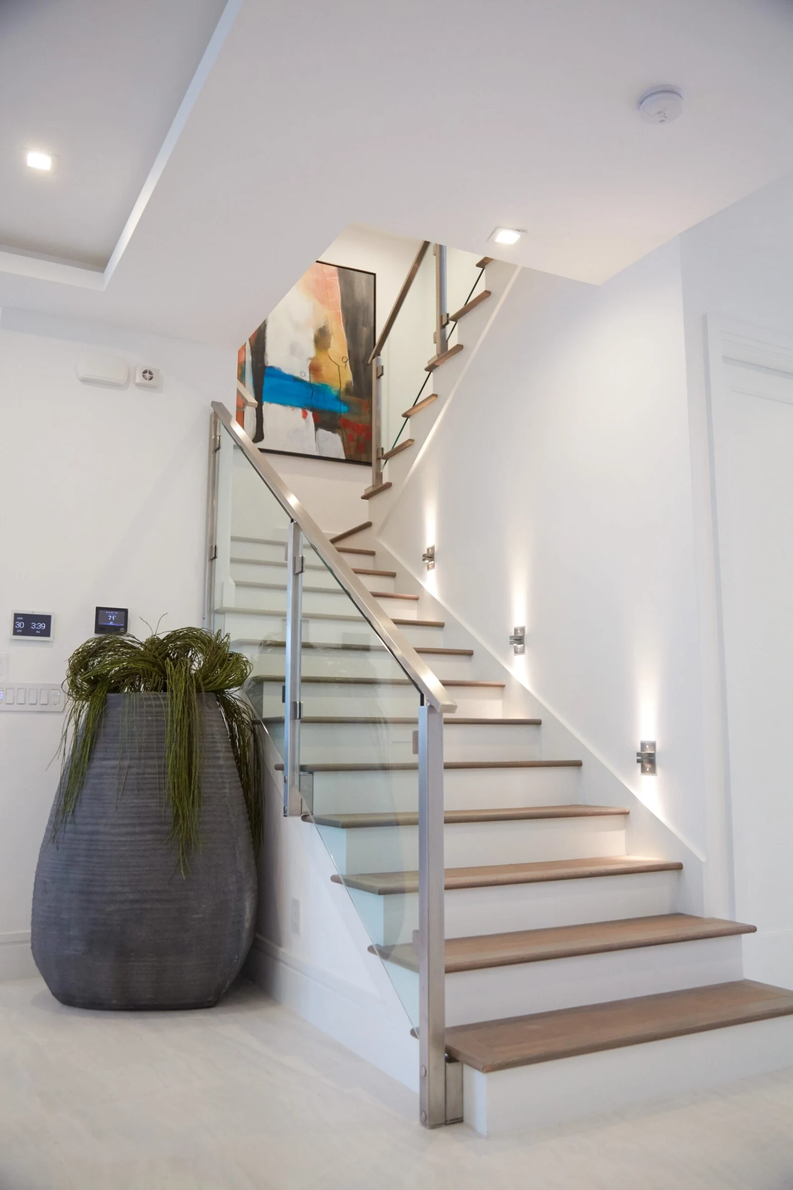 Curving stair with glass railing climbing a bright two-level entry beside a tall planter