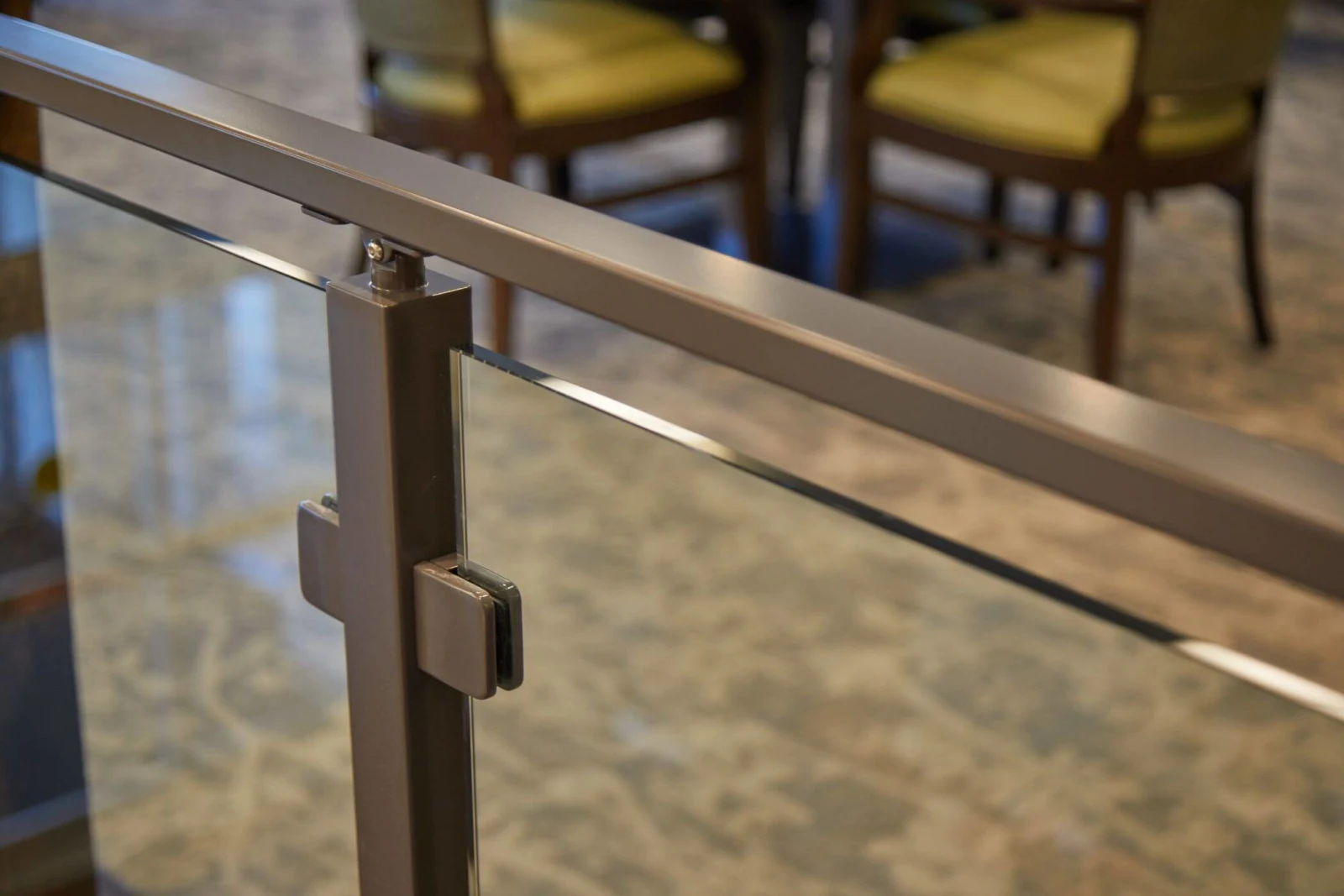 Close view of a post clamp gripping glass beneath a bronze top rail