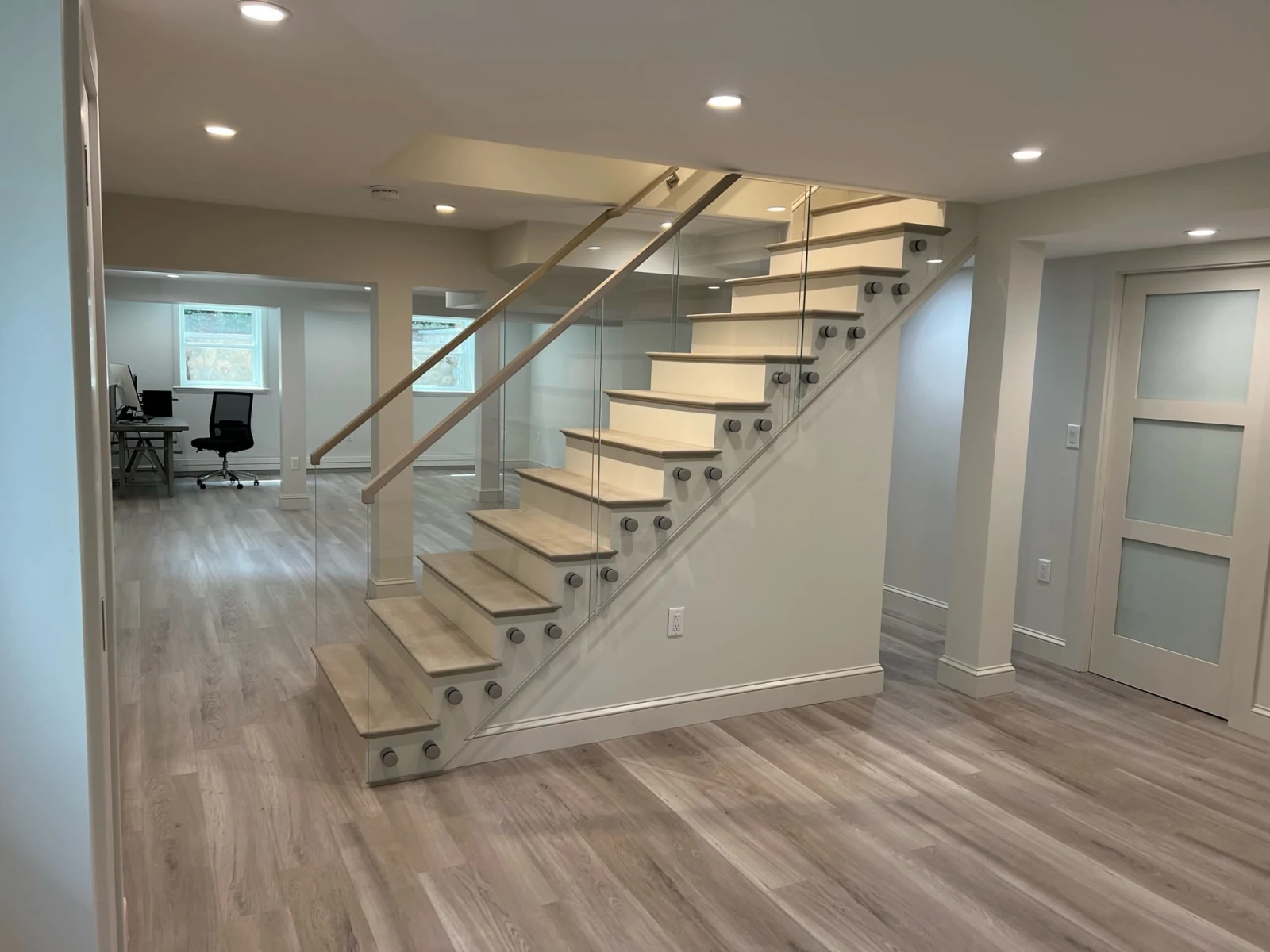 Round standoff pins fix glass to a straight stair in a finished lower level