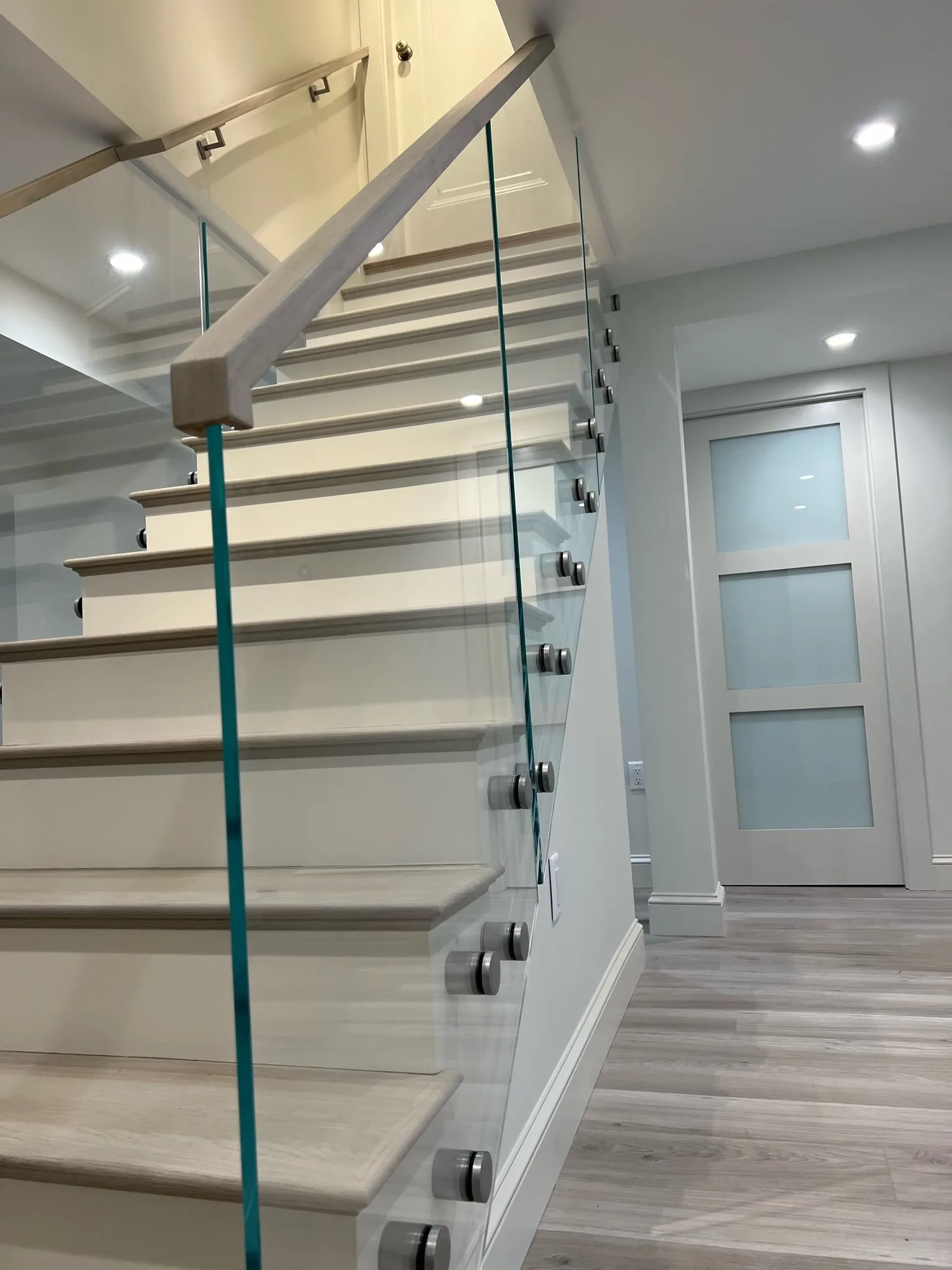 Glass panel on standoff pins running beside a stair with a wall handrail