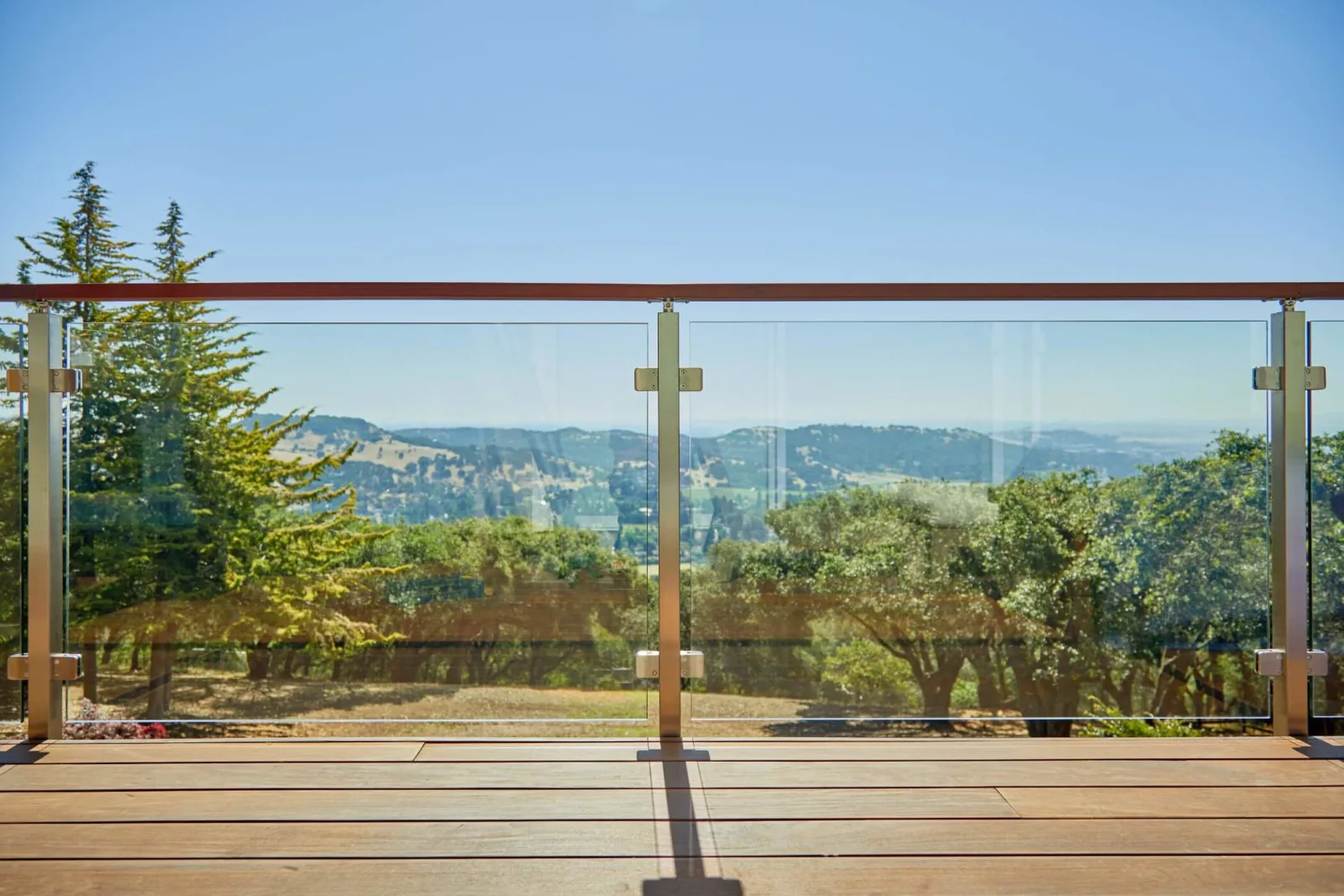 Wood-capped glass railing framing a broad view of hills and treetops