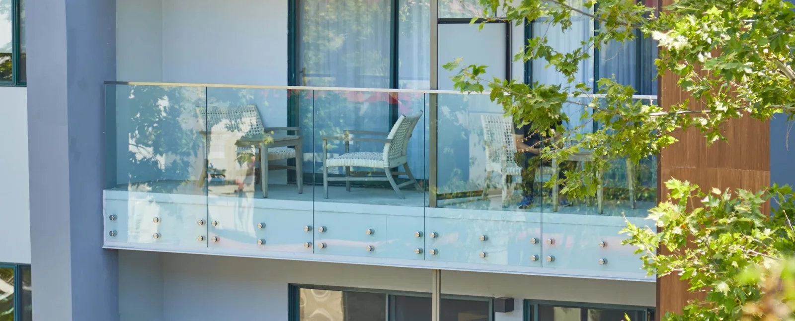 Building balcony edged in glass with patio chairs behind the panels