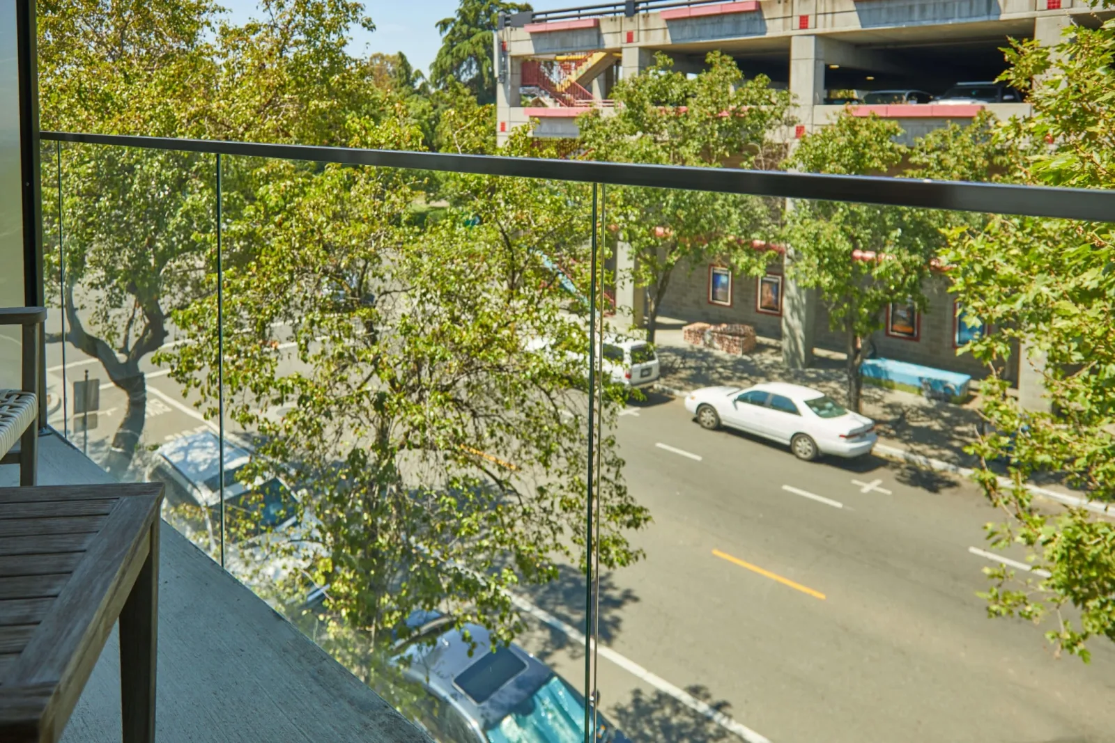 View from inside the balcony through the glass toward a tree-lined street