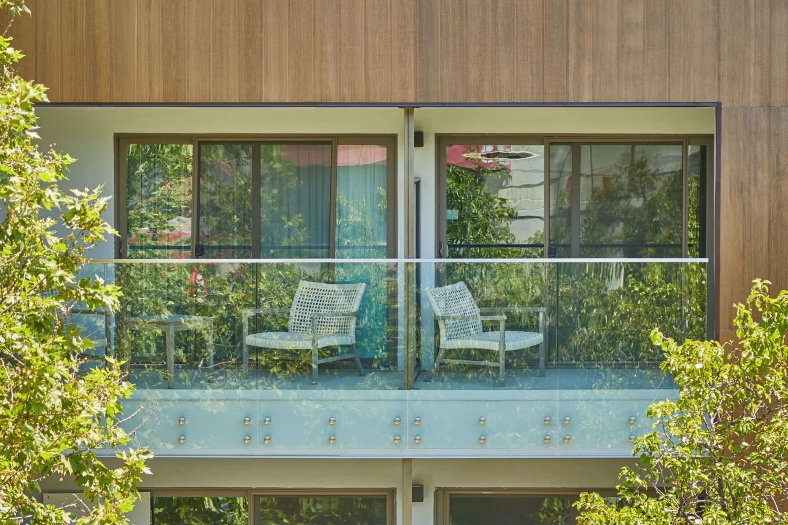 Frameless glass on standoff pins wraps a balcony of a wood-clad home among trees