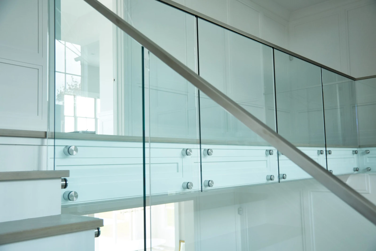Metal handrail crossing diagonally in front of glass and pale wood treads