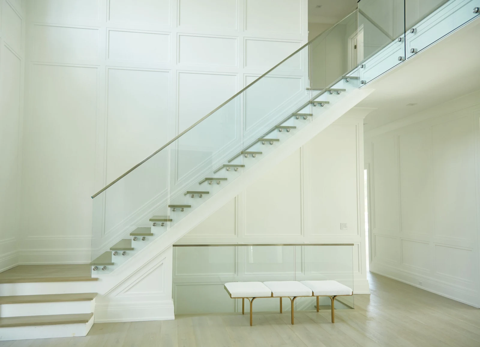 Slim top rail over glass beside a stair in a tall white paneled hall