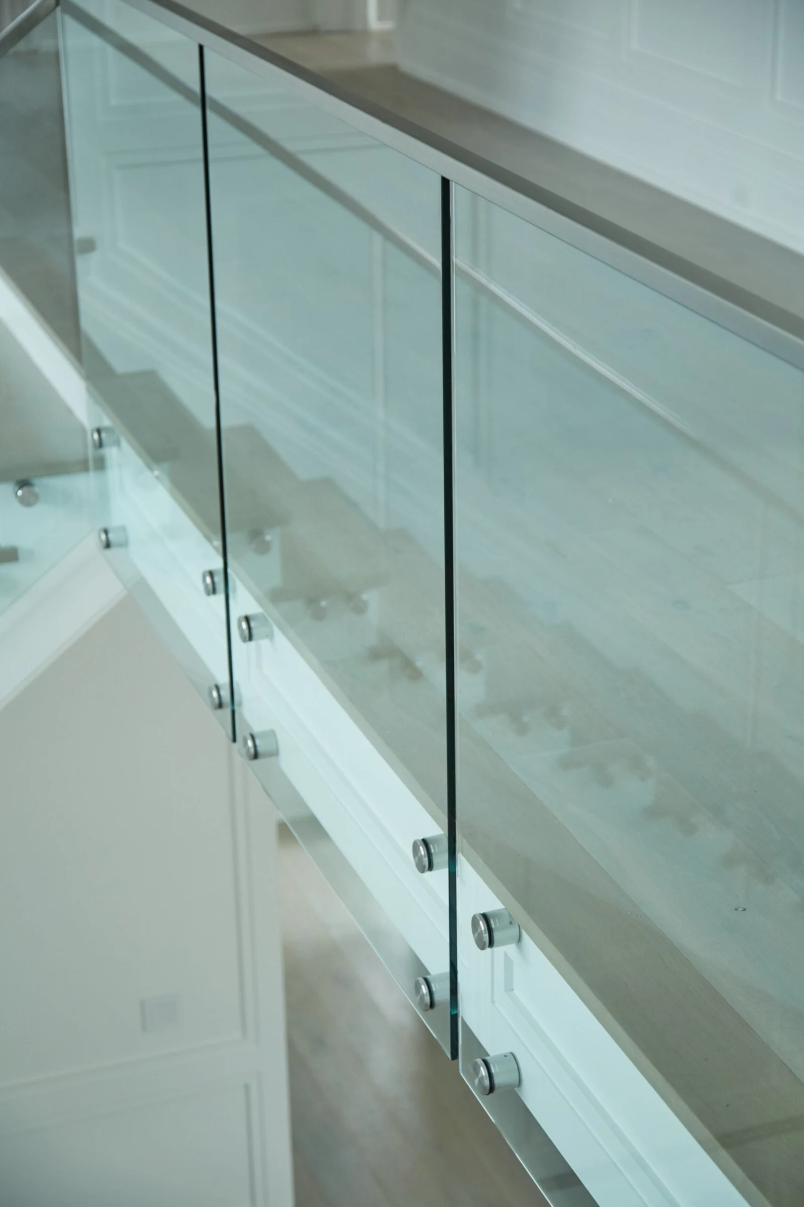 Glass panels mounted on standoffs against white paneled walls beside the stair