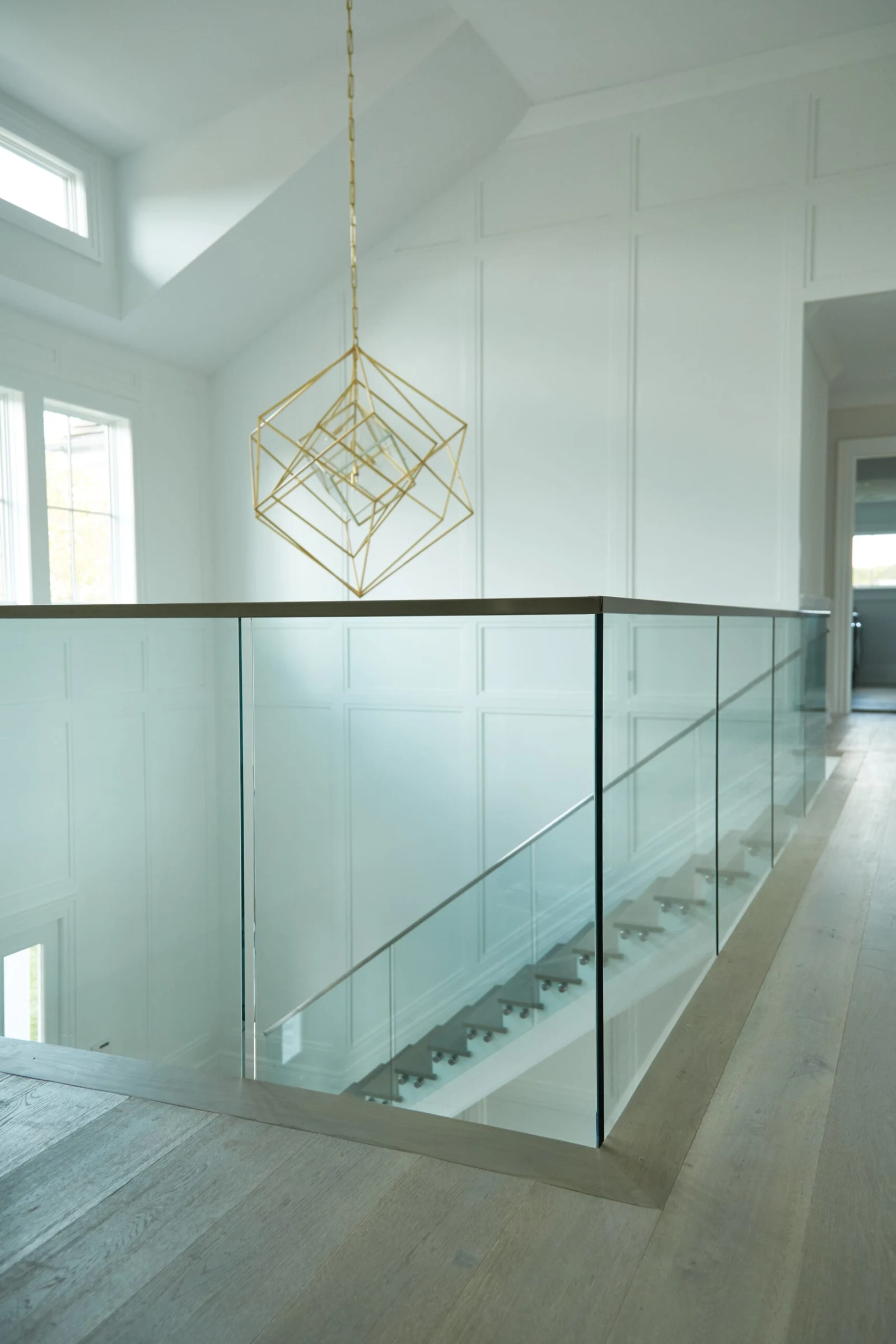 Upstairs hall lined with glass railing beneath a brass geometric pendant