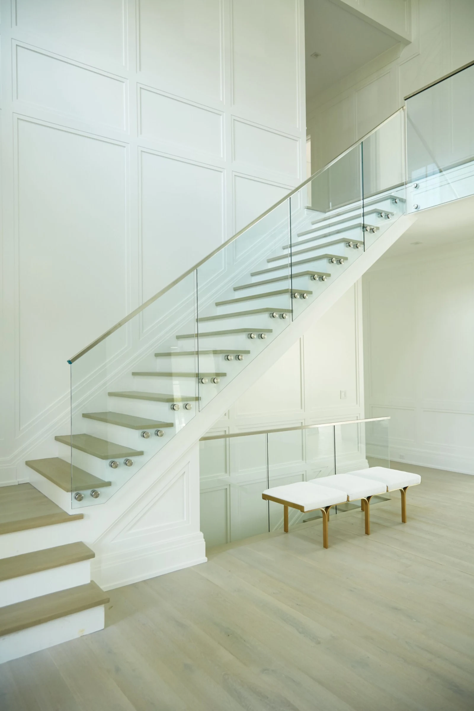 Curved flight rising along a paneled wall with glass railing and a bench