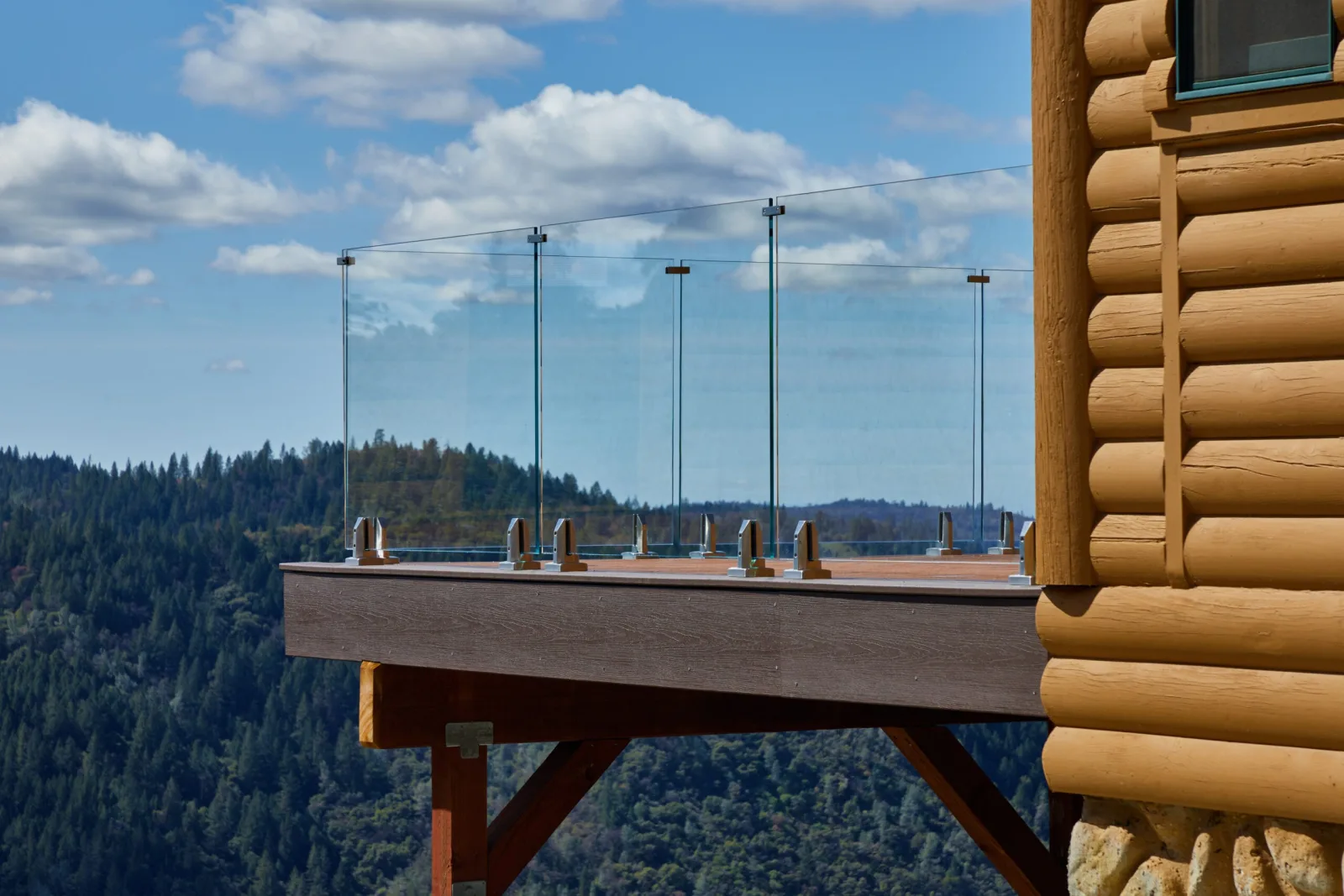 Cantilevered deck of a log home edged in glass above a valley