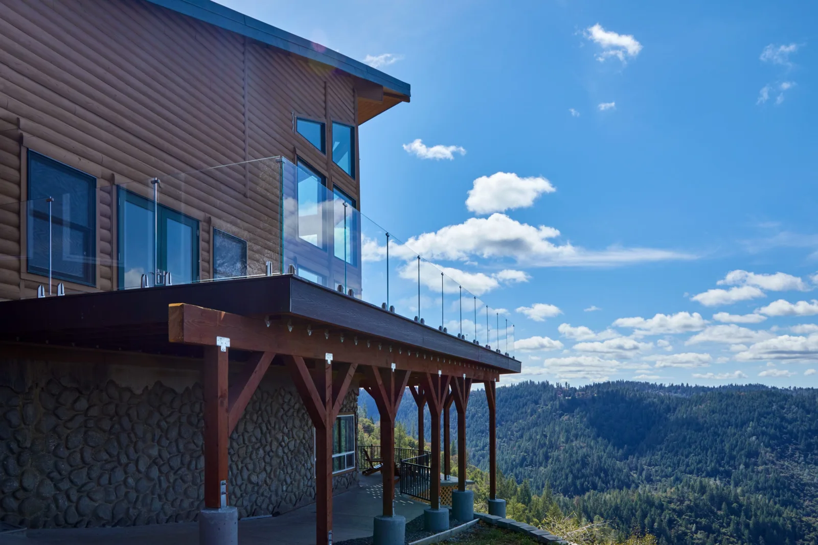 Timber posts supporting a wraparound deck whose glass railing catches the sunlight