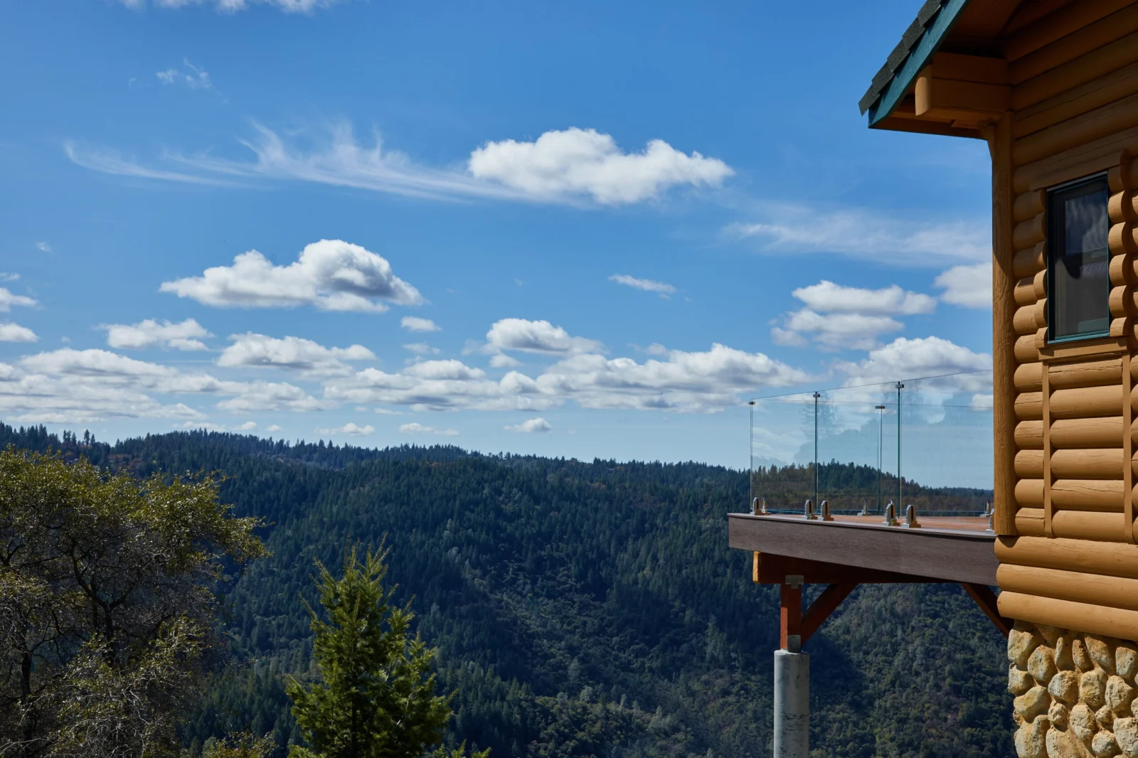 Log building corner and deck edge under a wide sky of scattered clouds