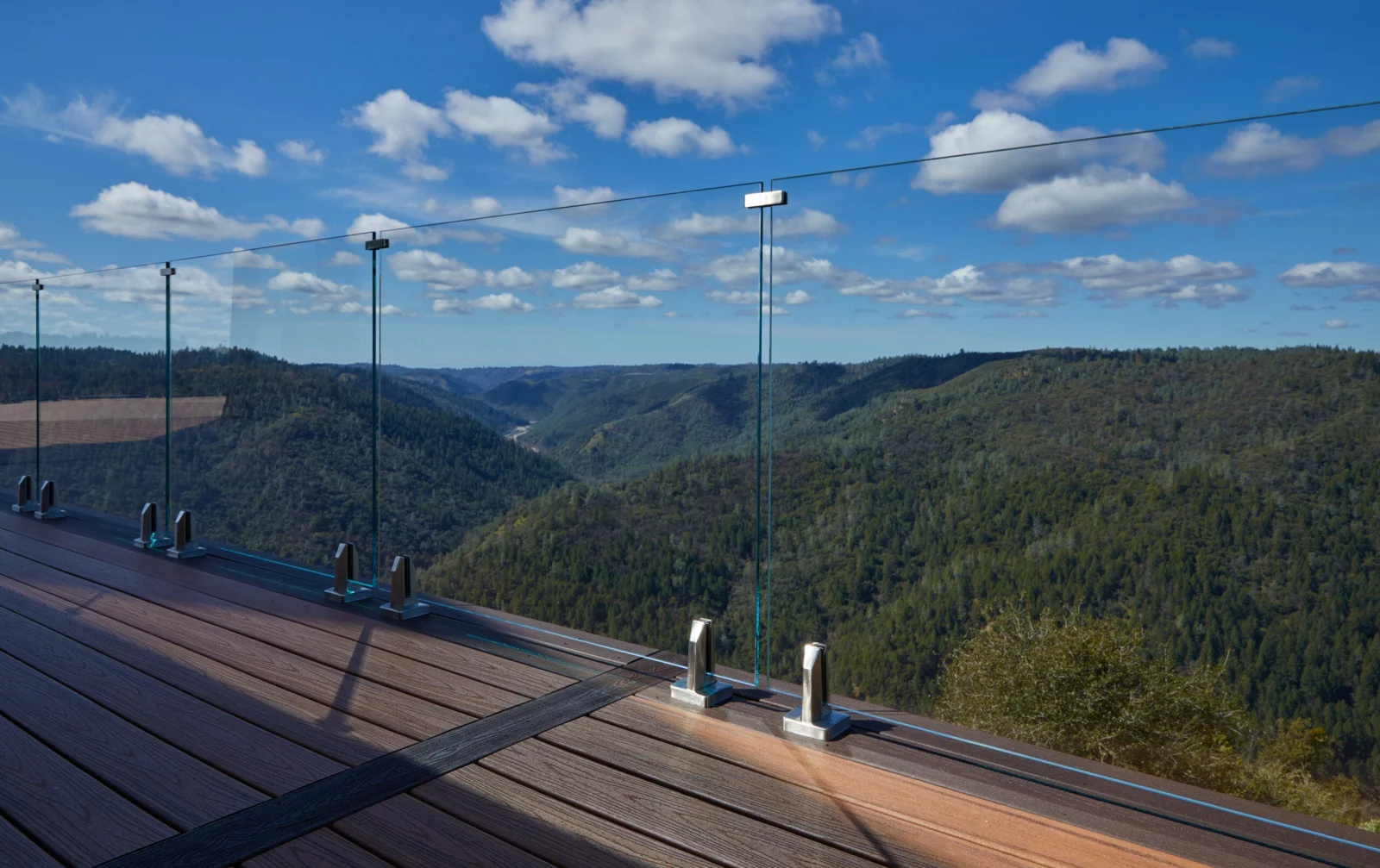 Frameless glass panels on base clamps edging a deck above forested ridges