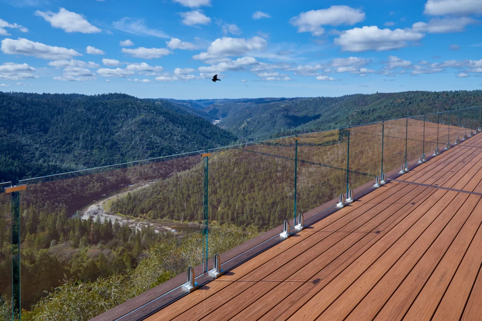 Wide deck edged in frameless glass on base clamps, high above a forested river valley