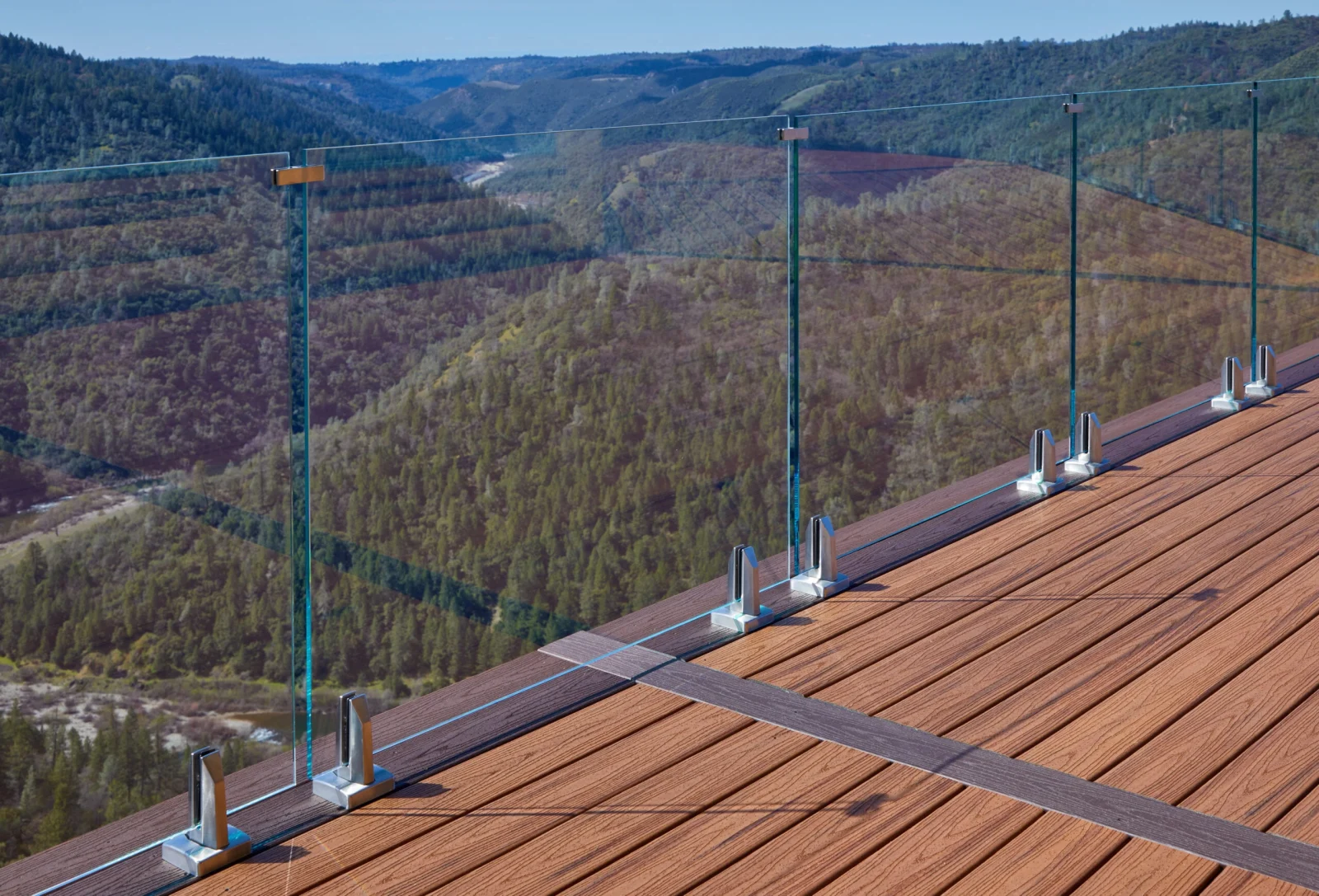 Base clamps spaced along the deck edge holding glass above a river canyon