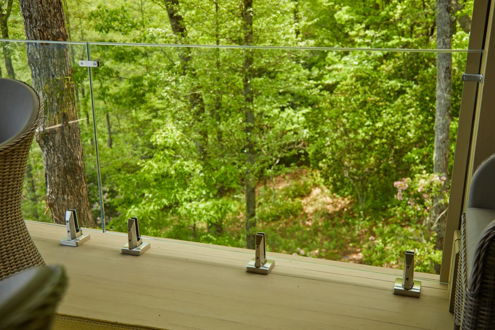 Row of base clamps anchoring glass along the porch edge amid green woods