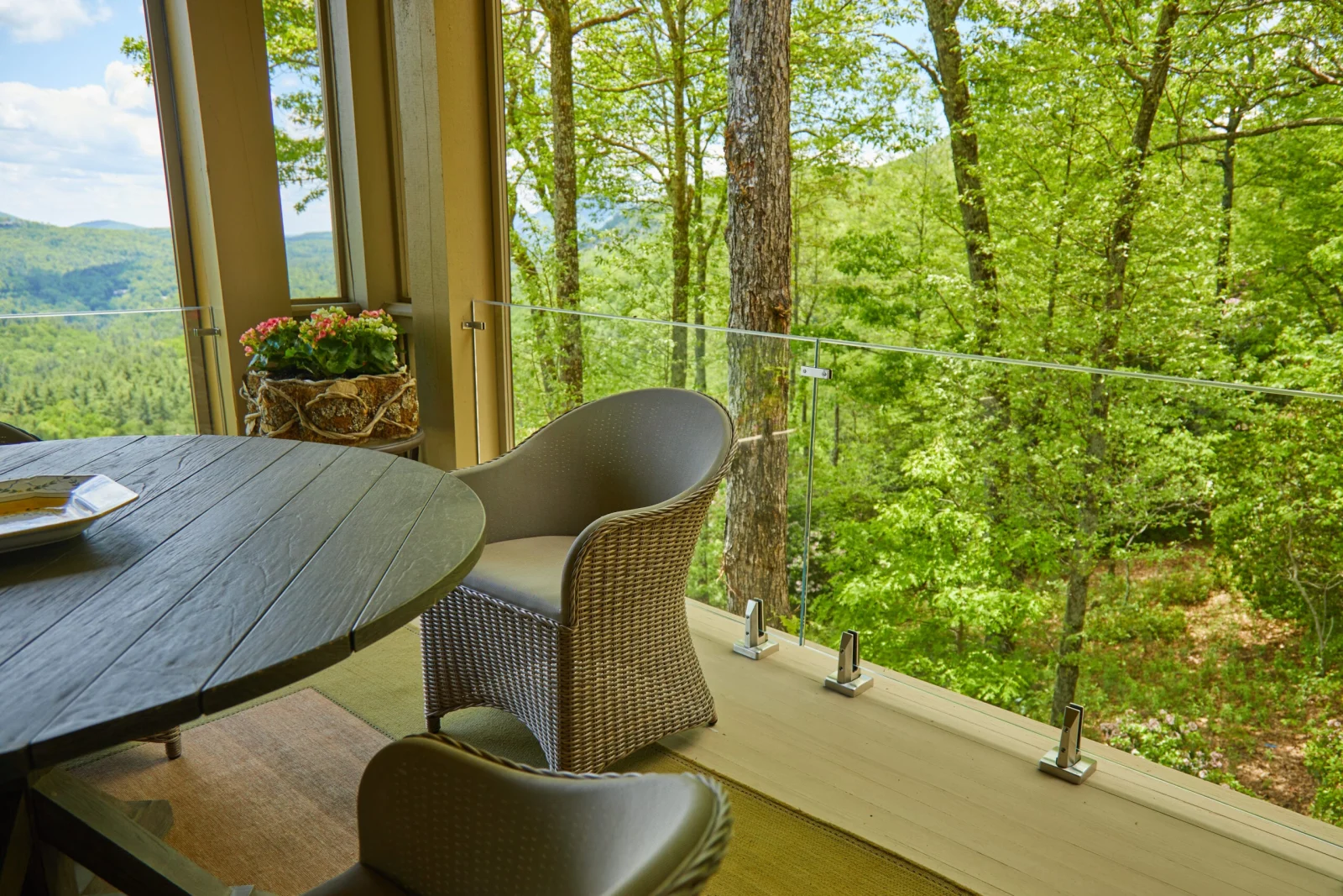 Wicker chairs and a round table on a porch behind clear glass panels