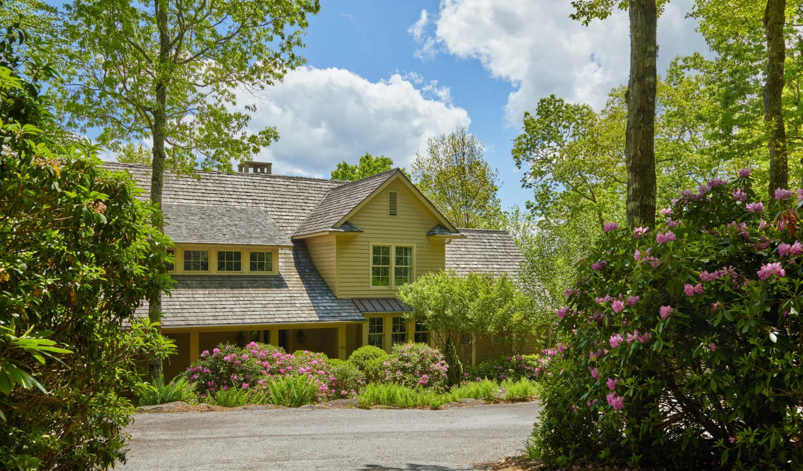 Shingled mountain house behind flowering shrubs at the end of a gravel drive