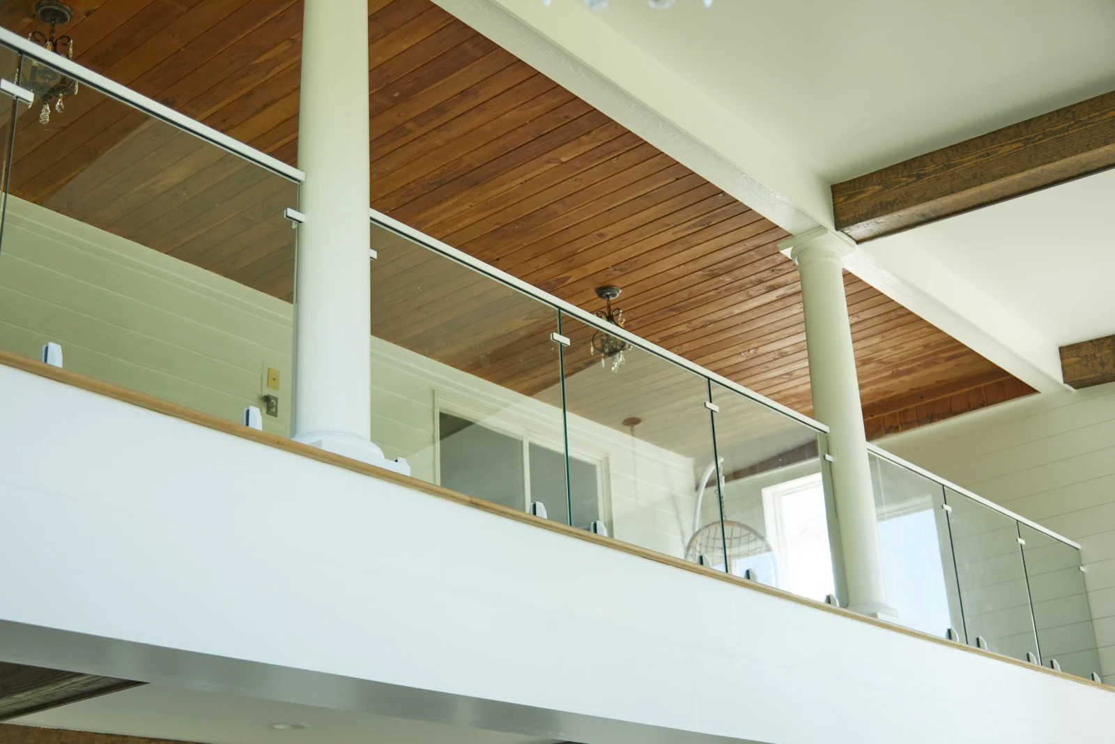 Upward view of a balcony glass railing with wood top rail beneath a plank ceiling
