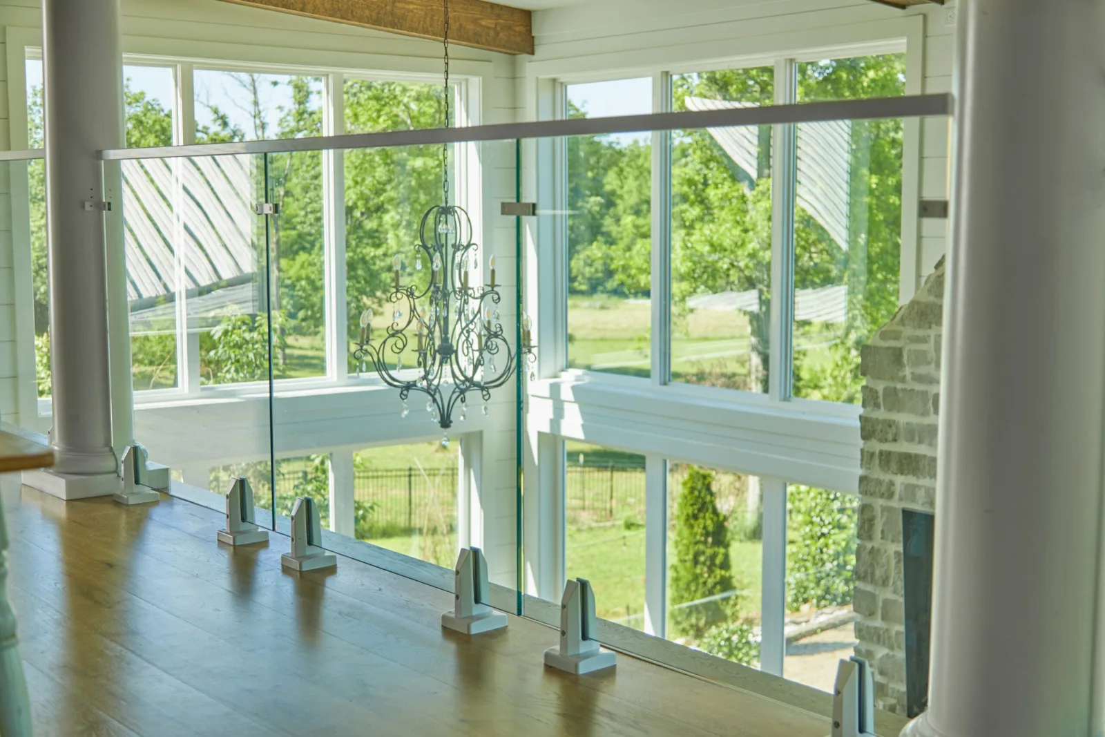 Silver base clamps hold glass along a loft edge above tall windows and a chandelier