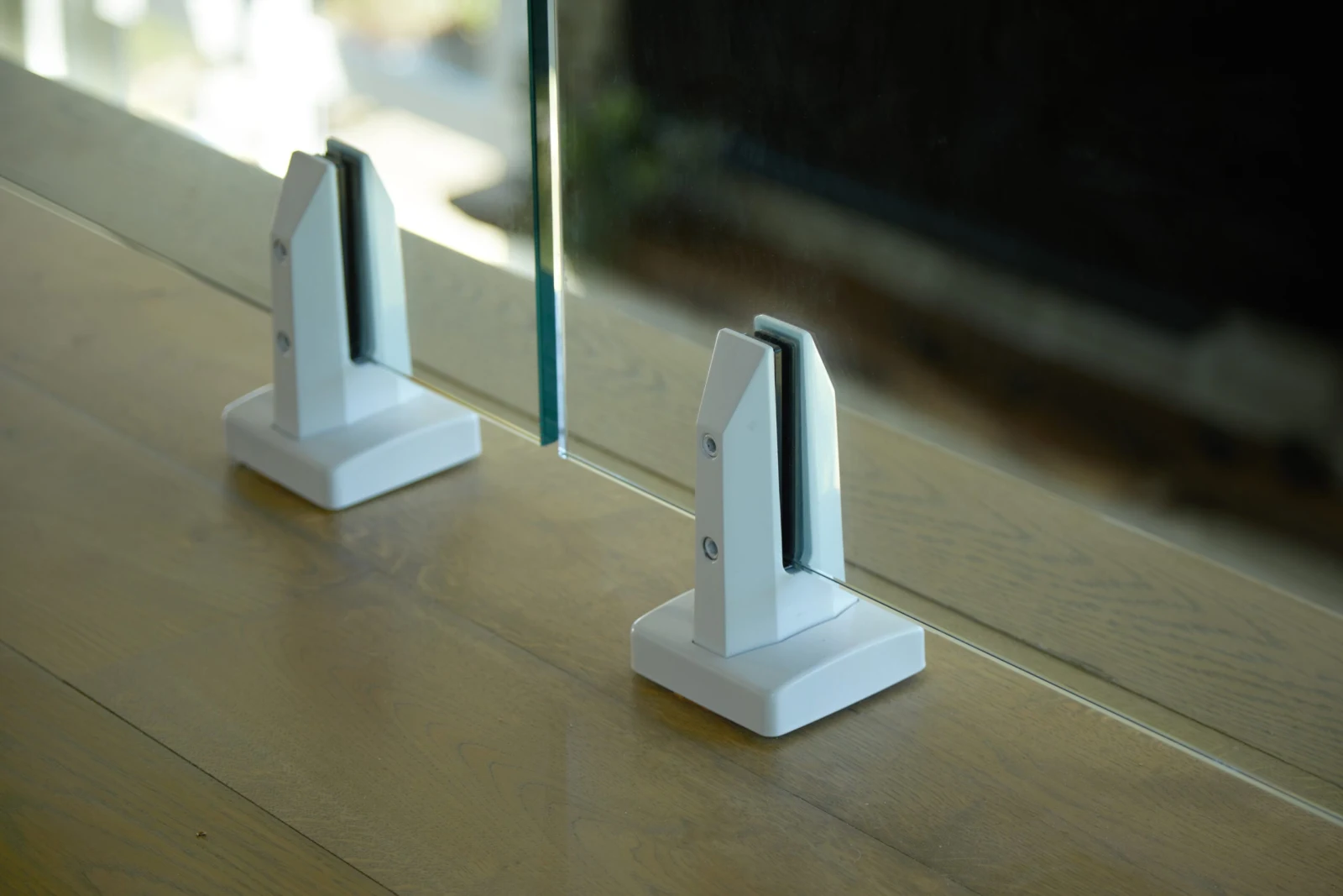 Close view of two white base clamps gripping a glass panel on wood flooring