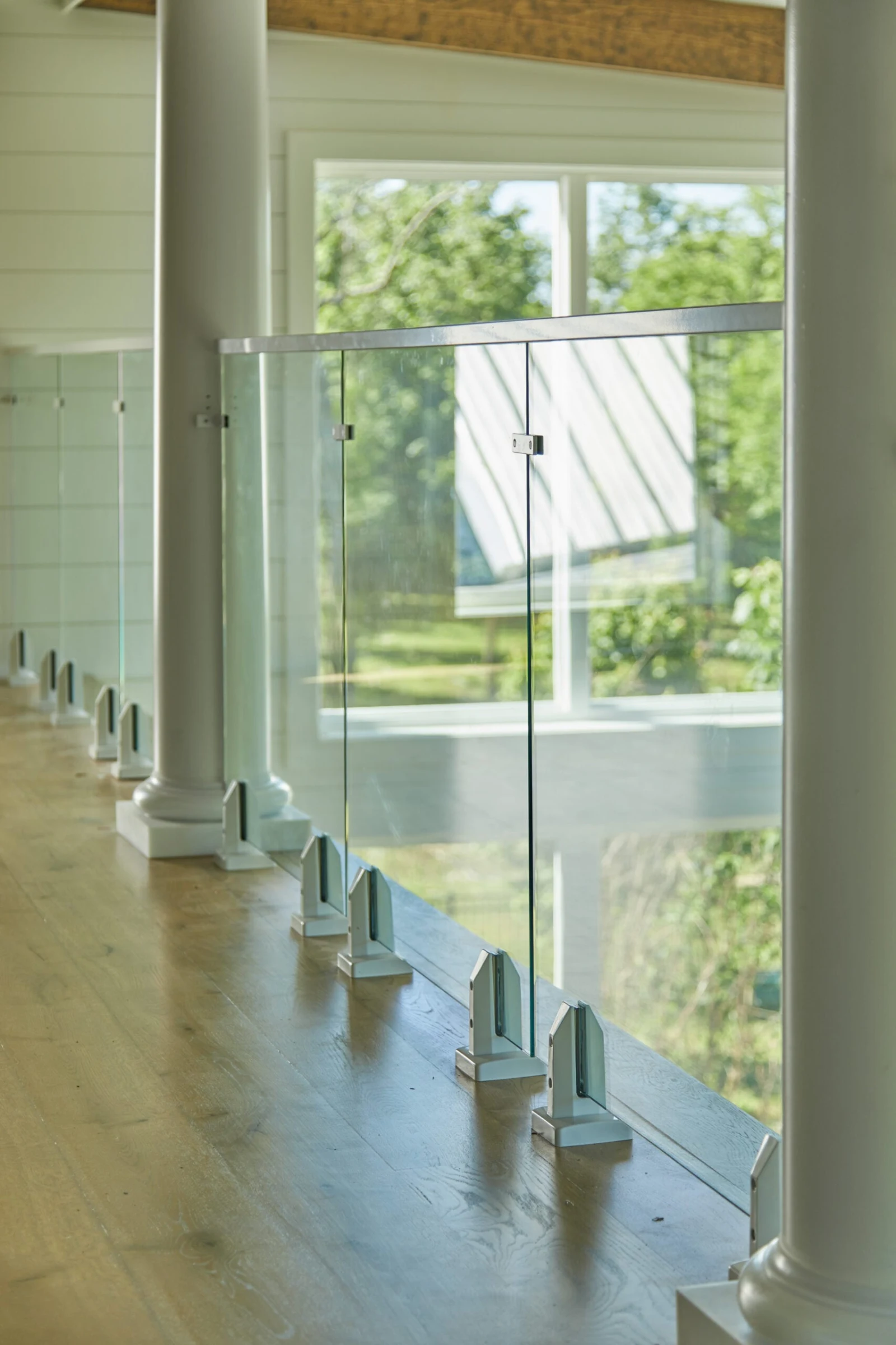 Frameless glass panels in white base clamps line a second-floor walkway beside tall windows