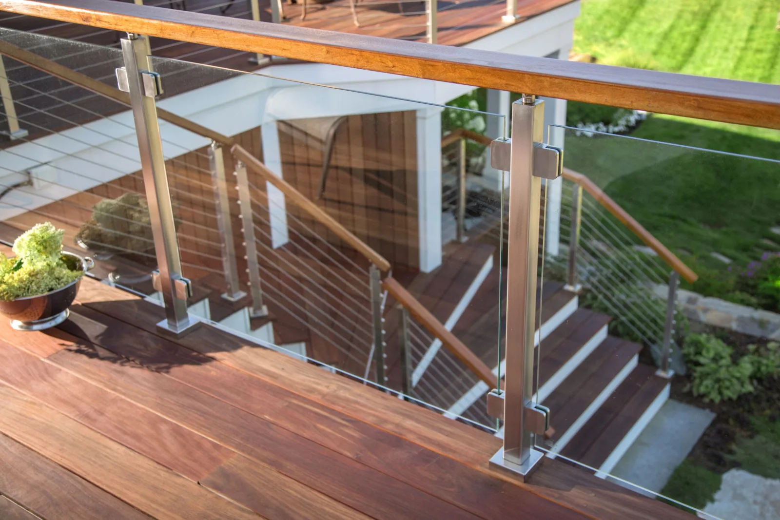 Glass deck panels and wood top rail meet a cable-infilled stair descending to the lawn