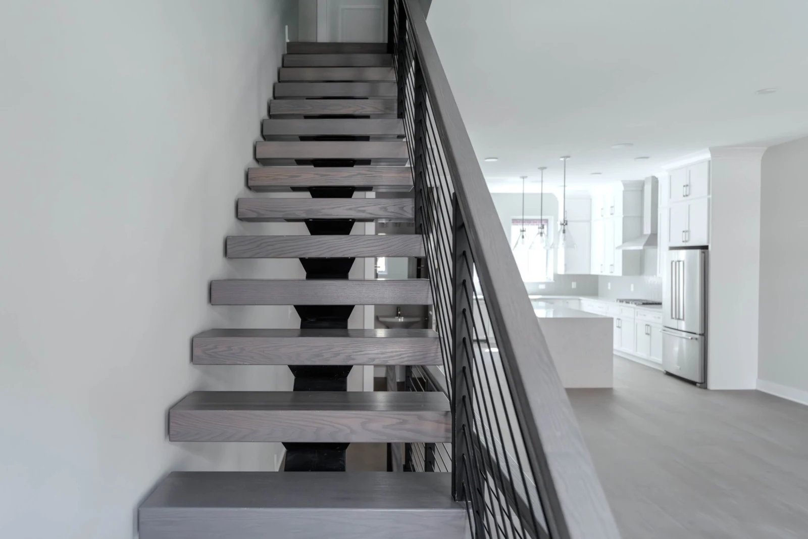 Floating treads on a black center stringer with black rod railing beside a white kitchen
