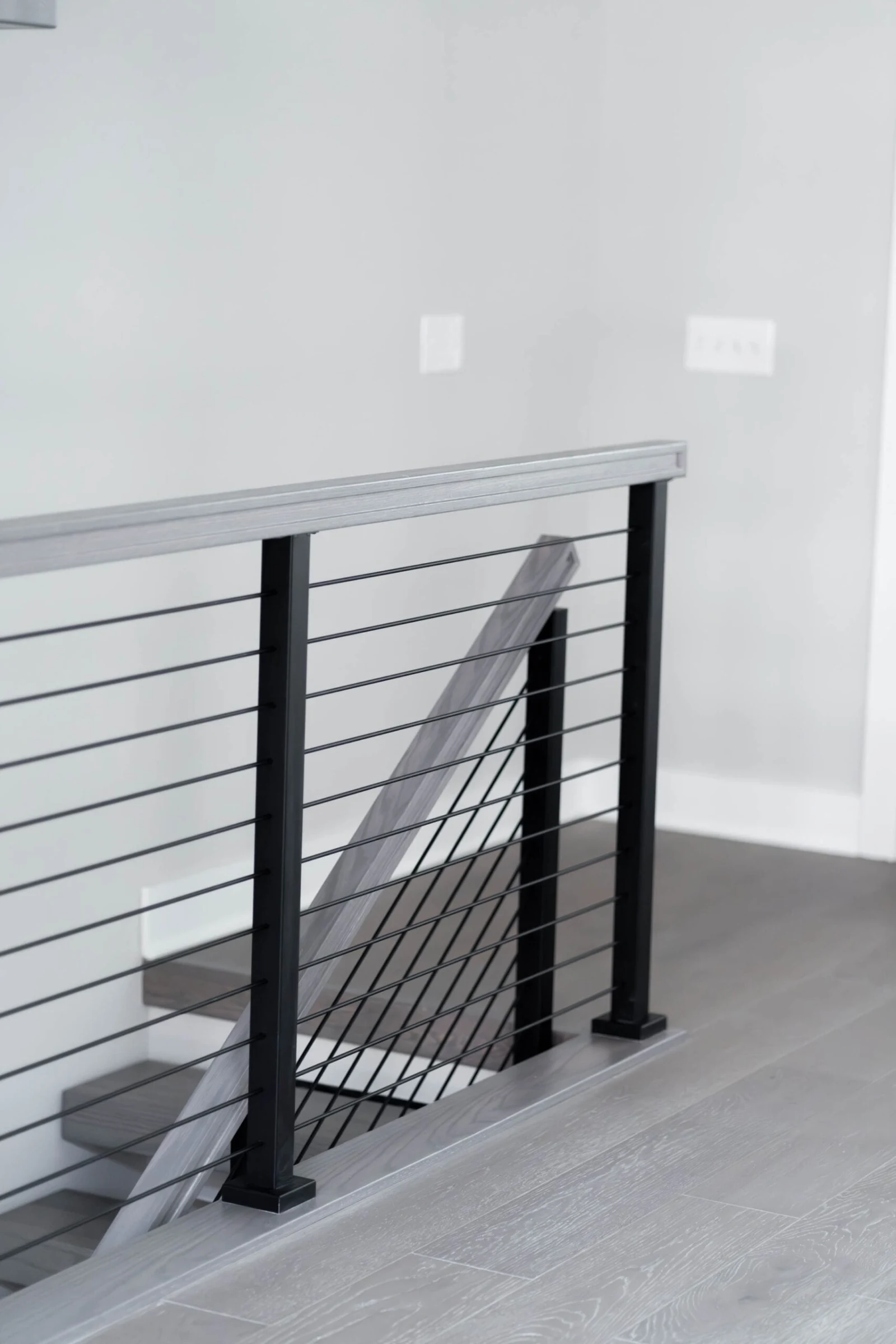 Short balcony guard of black posts and horizontal rods capping the stair opening