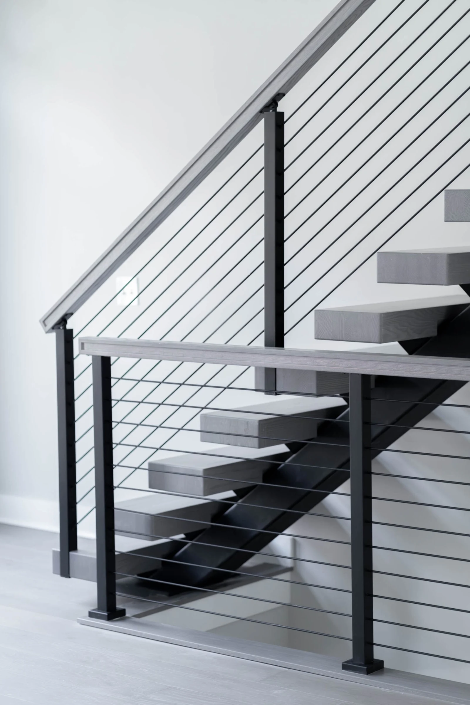 Underside view of cantilevered gray treads carried by one black stringer behind rod railing