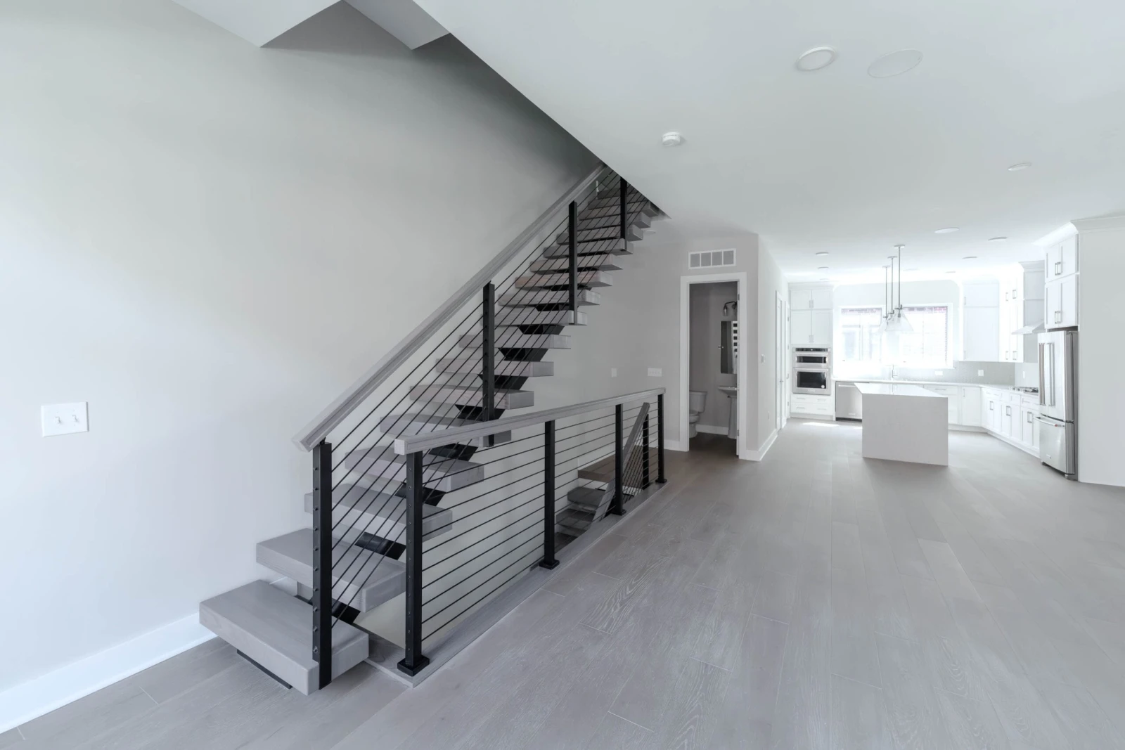 Open living area with the stair and rod railing at left and kitchen beyond