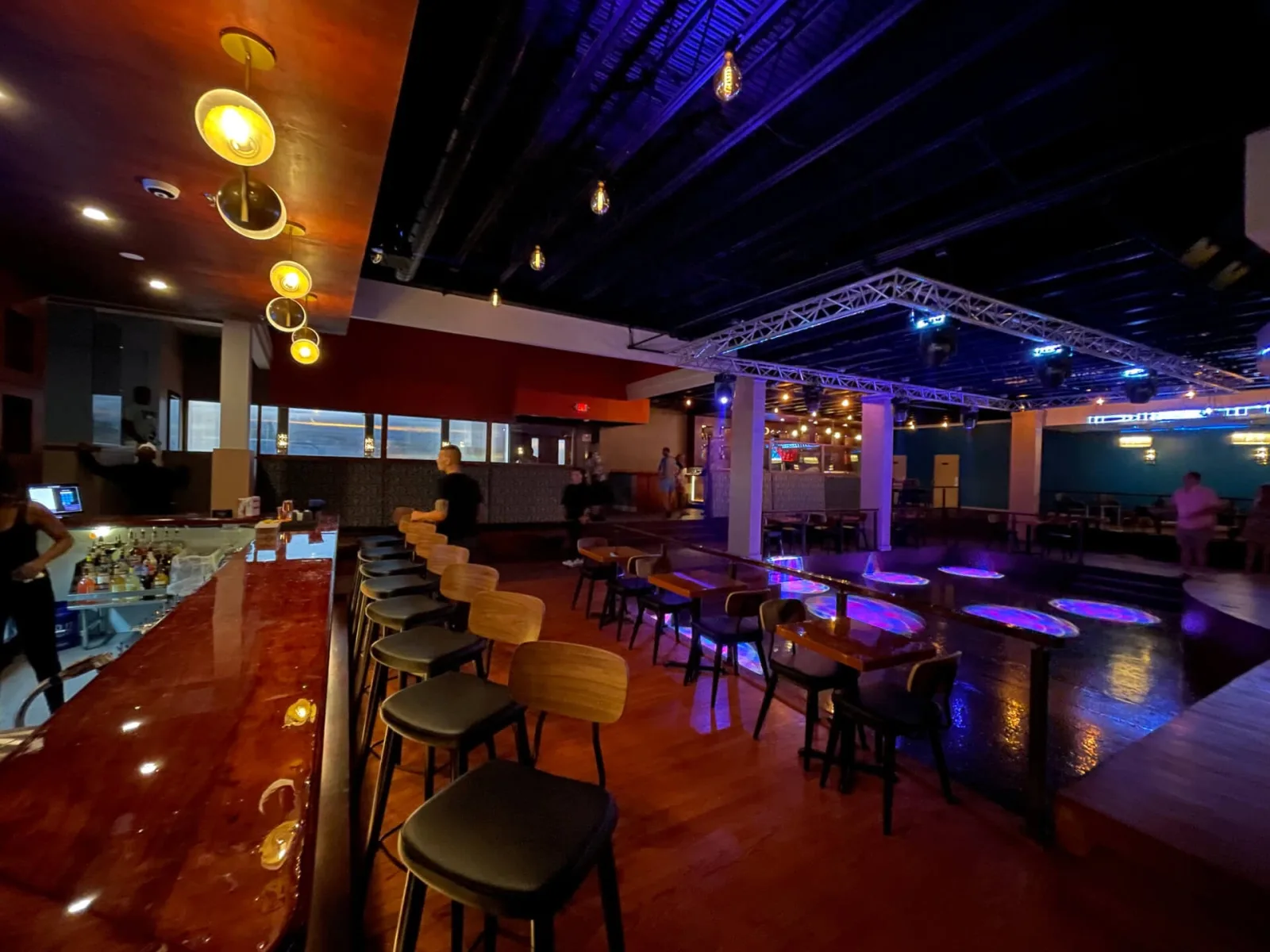 Long bar with stools under blue ceiling lighting and pendant lamps along the room