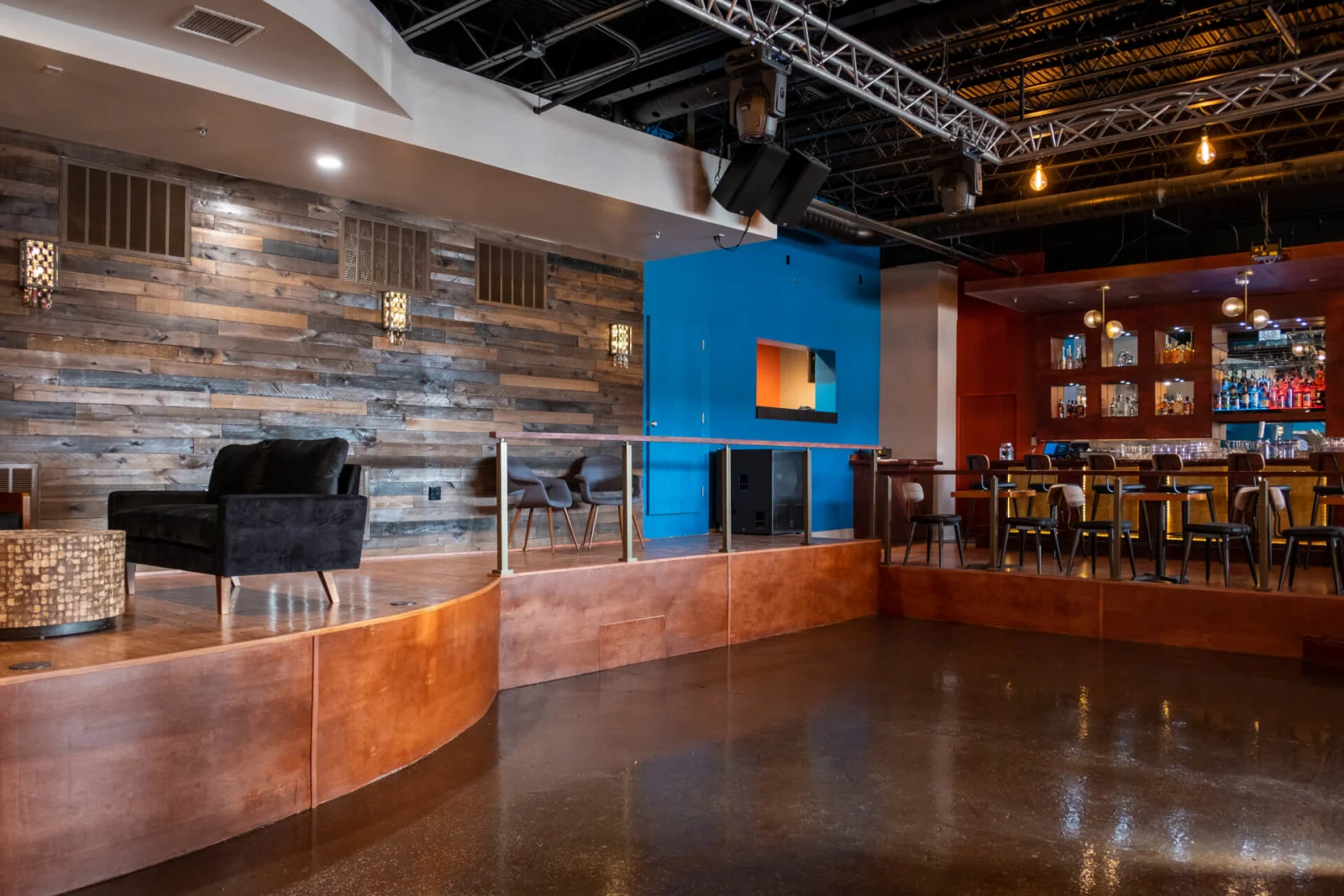 Curved raised lounge with black railing, armchairs and a plank wall beside a bar