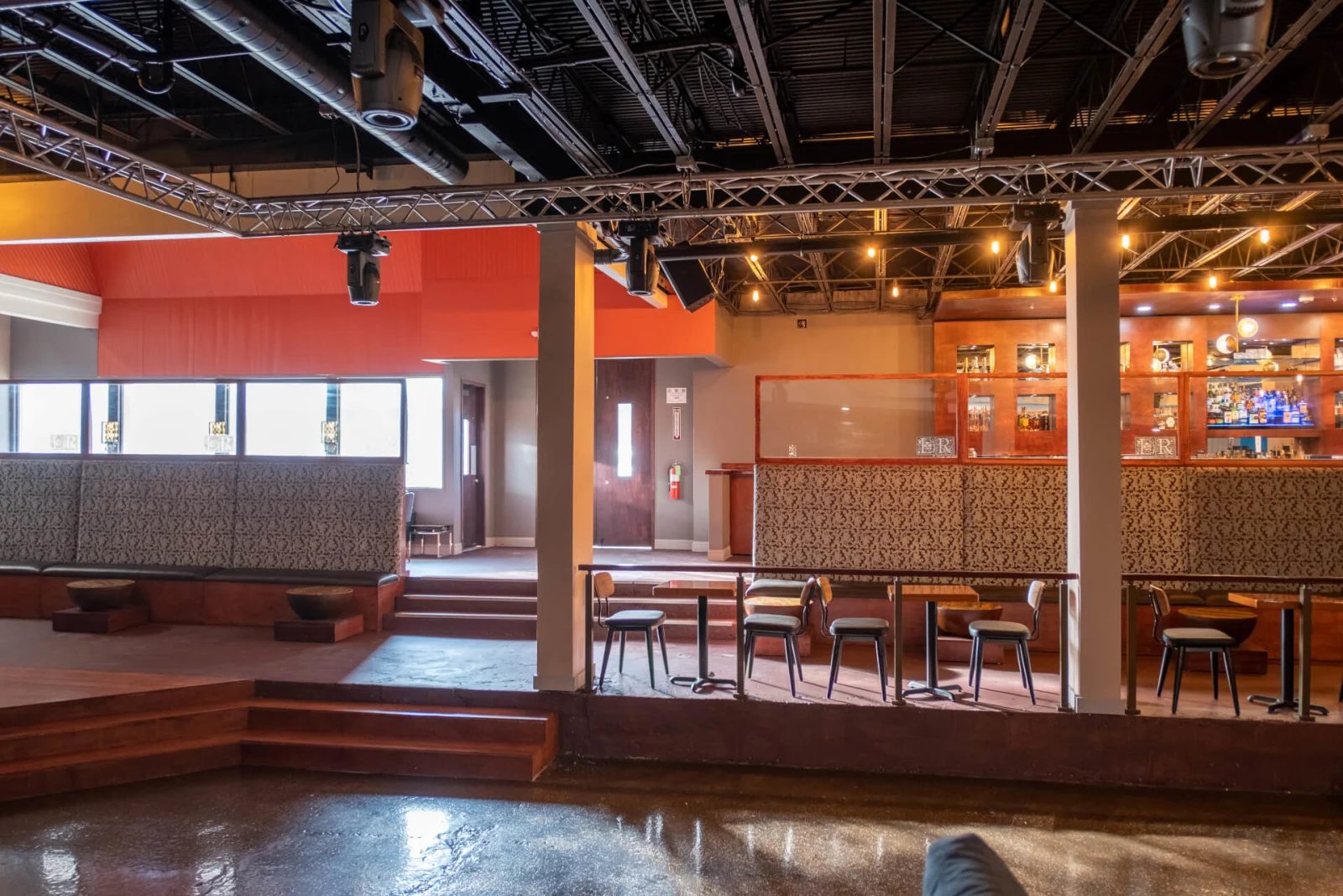 Orange-walled lounge with high-top tables, a low stage and a railed platform edge