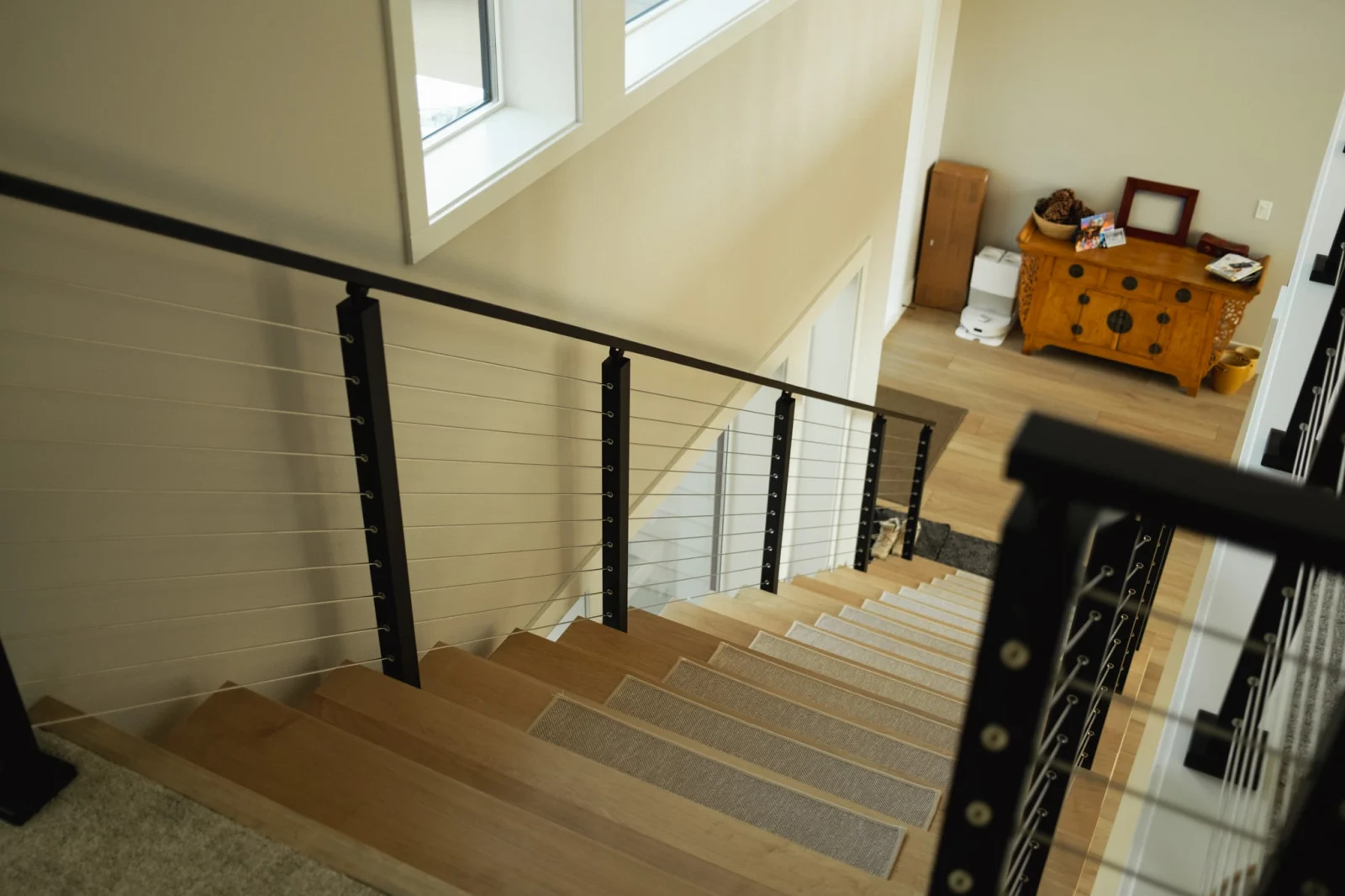 Looking down a stair runner between black posts strung with horizontal cable