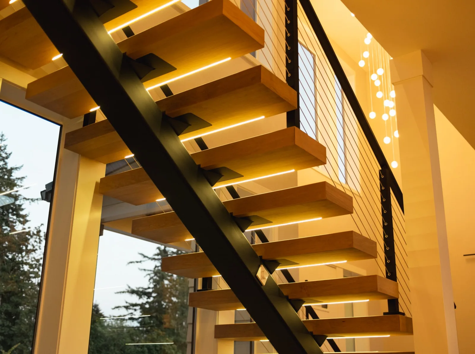 Looking up at floating treads with LED strips glowing beneath, cable railing above
