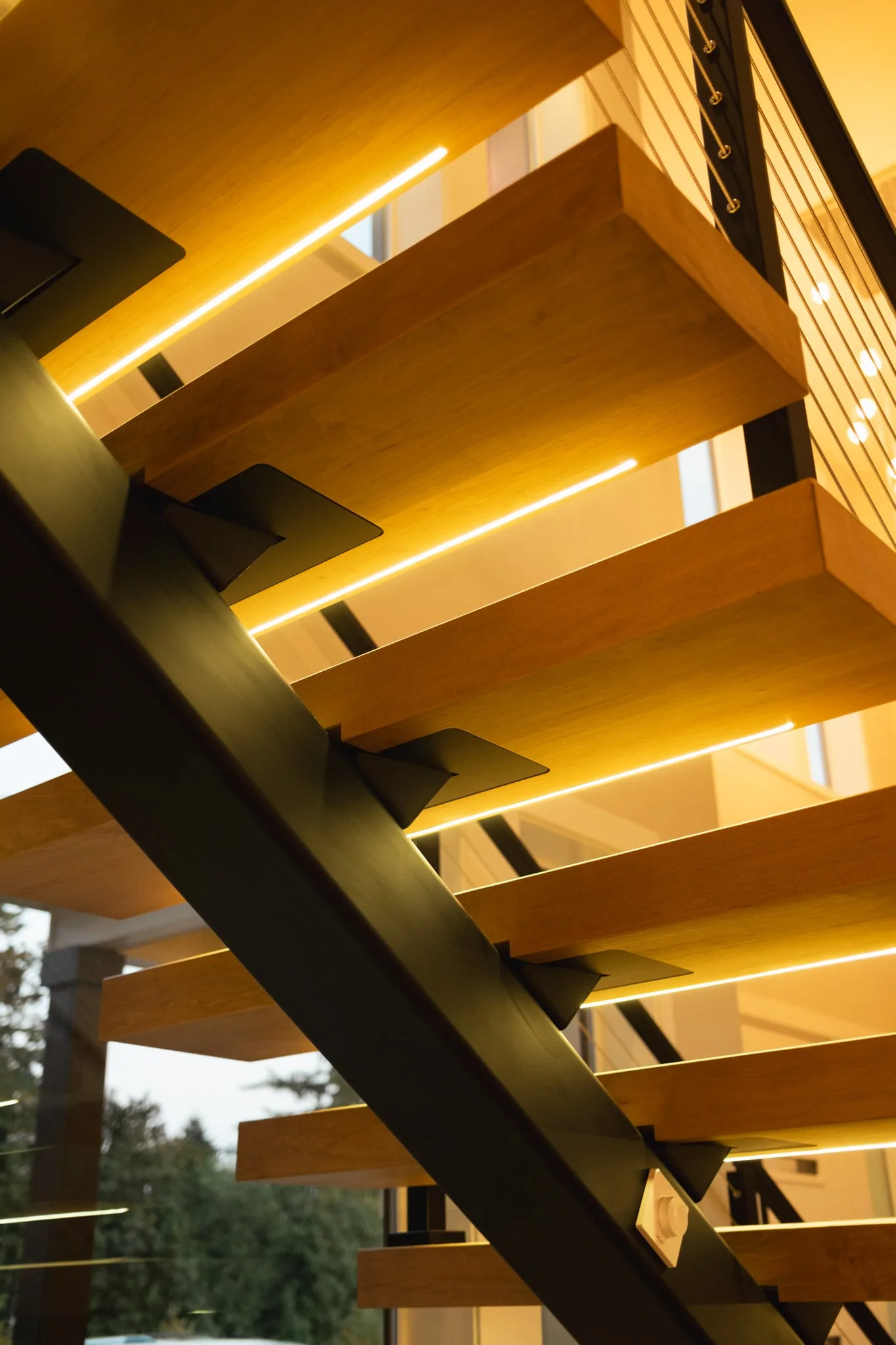 Underside of a floating stair with LED strips glowing beneath each wood tread