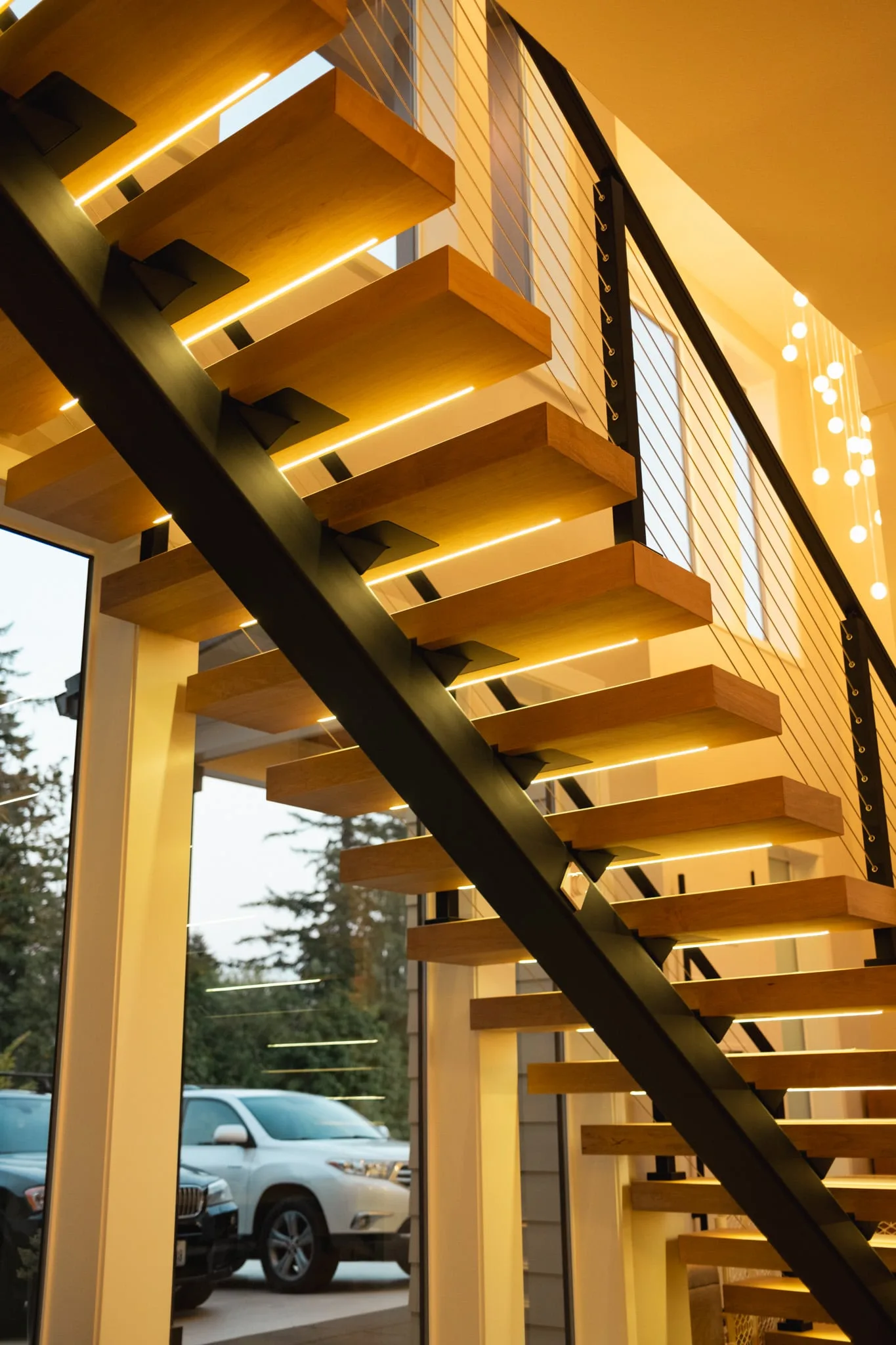 LED-lit stair climbing a black stringer with cable railing above a covered entry