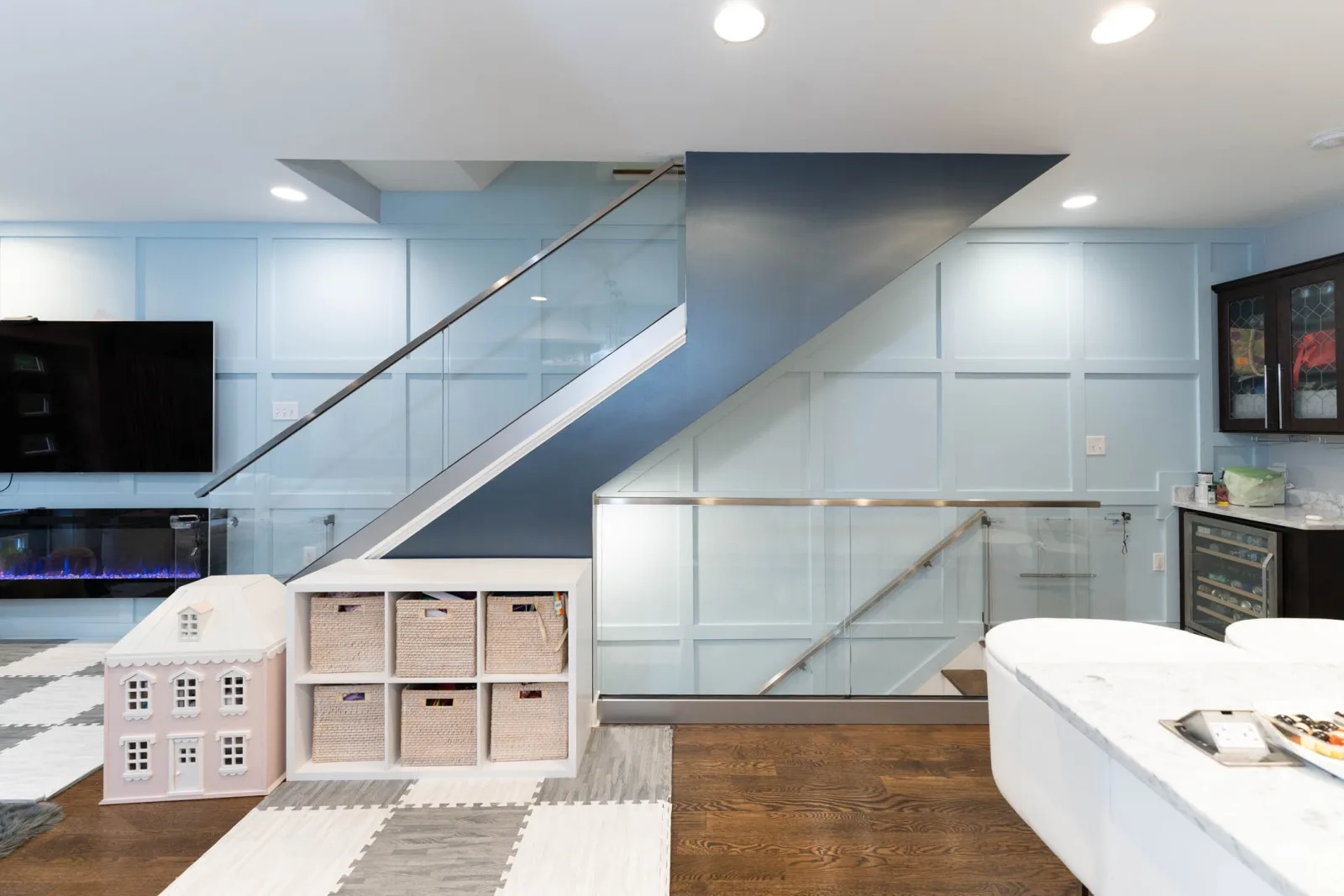 Glass railing wrapping a stairwell opening in a paneled basement family room